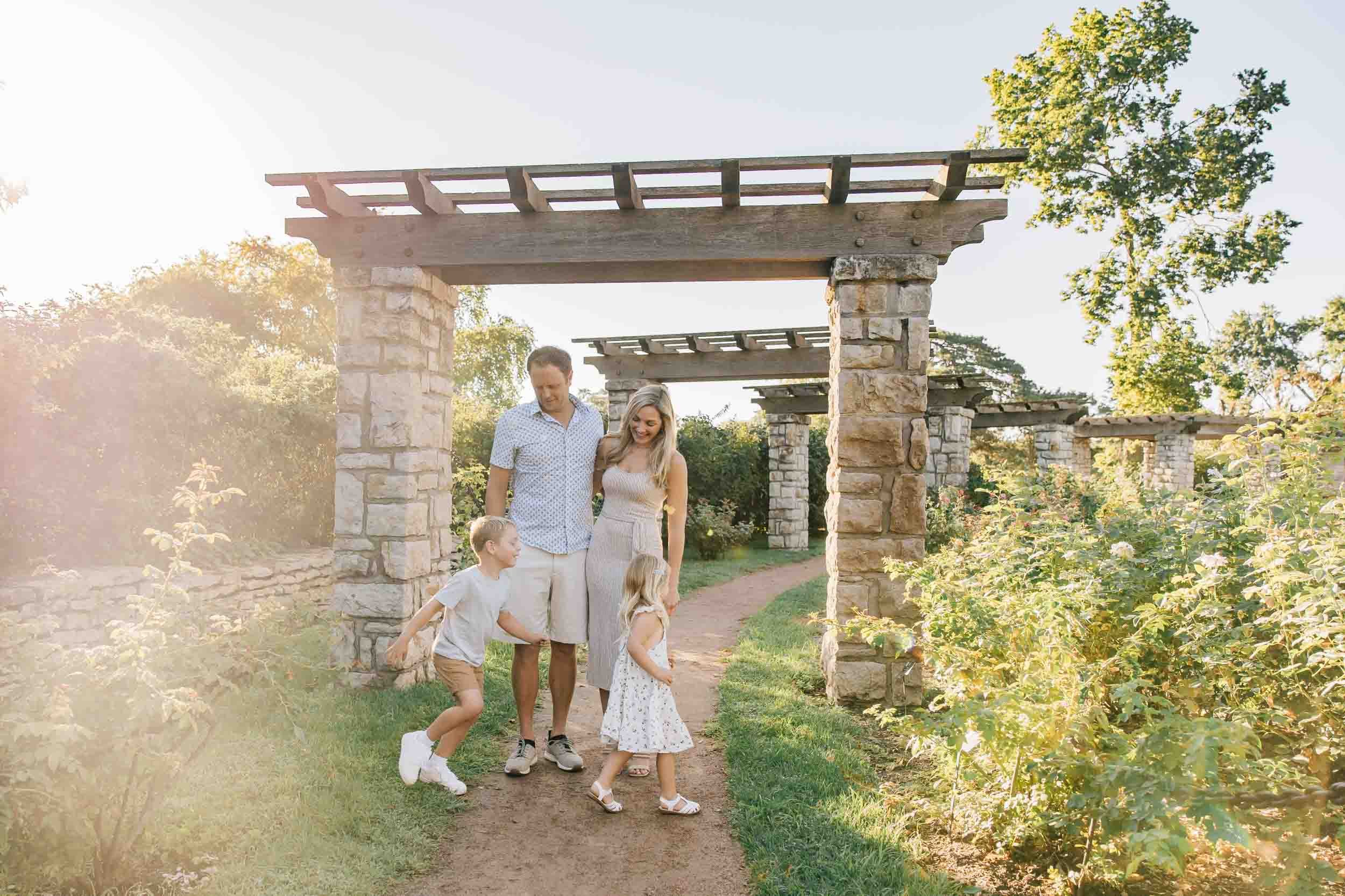 family walking through a stone pergola pathway surrounded by roses