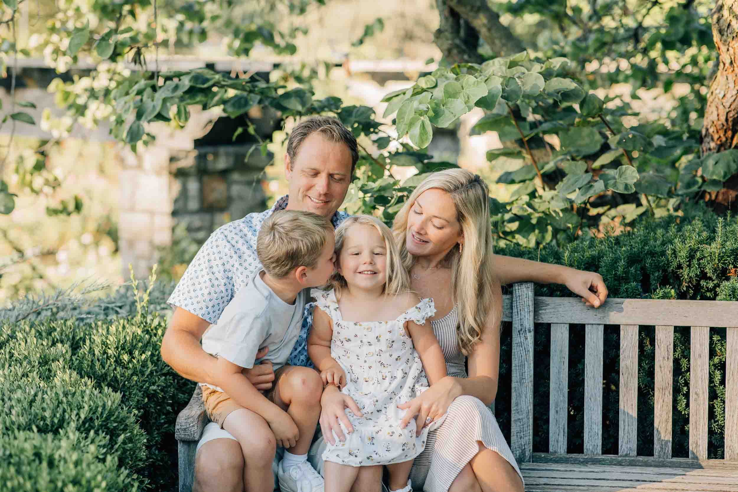 family of four snuggled together at a garden bench