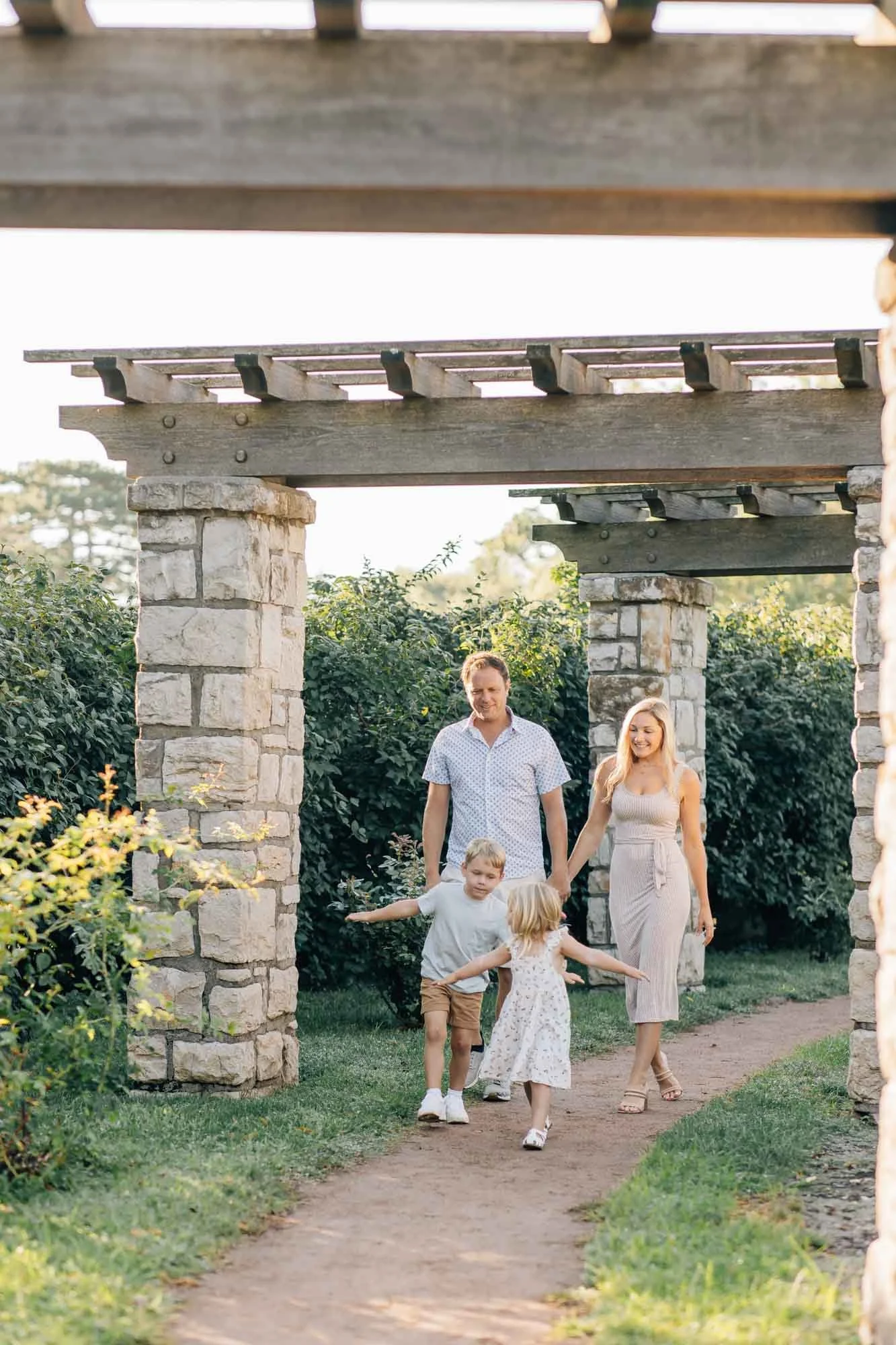 family of  four walking hand in hand through a stone garden pergola