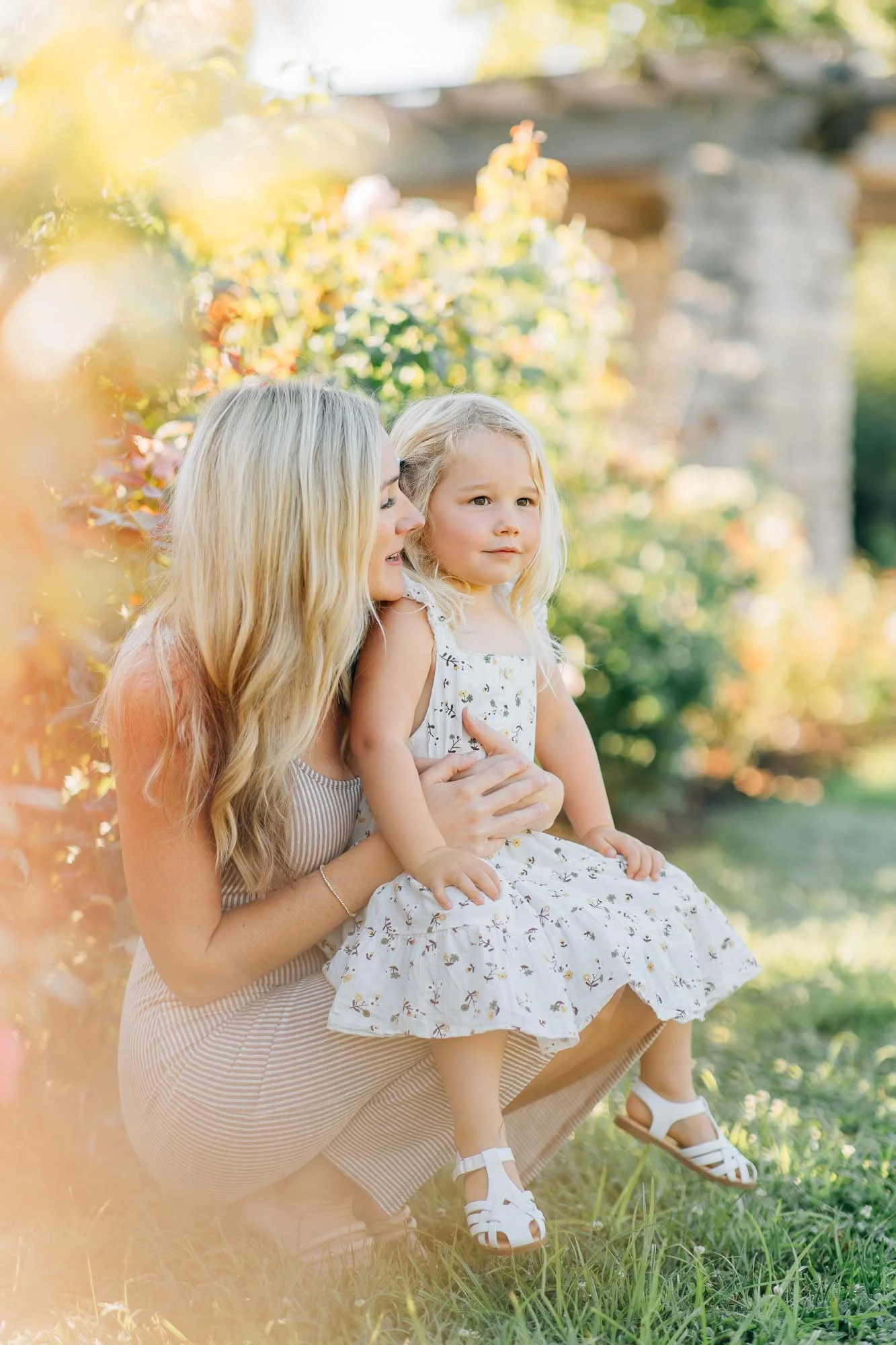 mother holding her daughter while both smiling in the sun