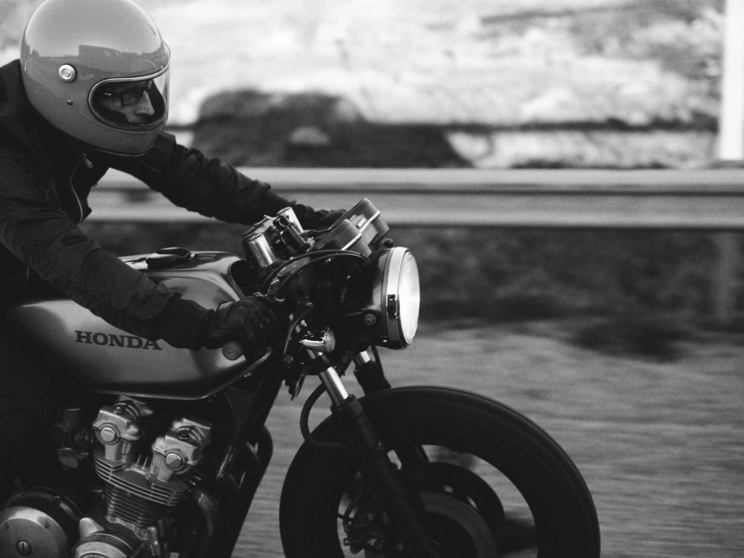 Motoristi ajaa Honda-moottoripyörää kypärä päässä. Kuva on mustavalkoinen.