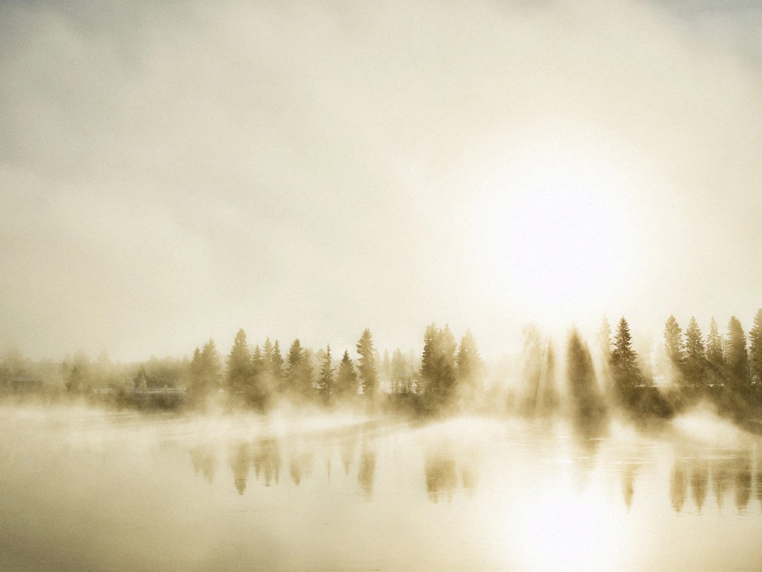 Sumuinen aamu metsäjärvellä, taustalla nouseva aurinko, joka luo kultaisia säteitä veden yllä.