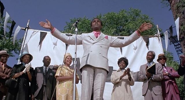 At a rally in Harlem, &quot;Reverend&quot; Deke O'Malley (Calvin Lockhart) selling shares for the purchase of a ship to take Blacks back to Africa in the 1970 film 'Cotton Comes to Harlem.' Based upon the 1965 hardboiled crime novel of the same name 