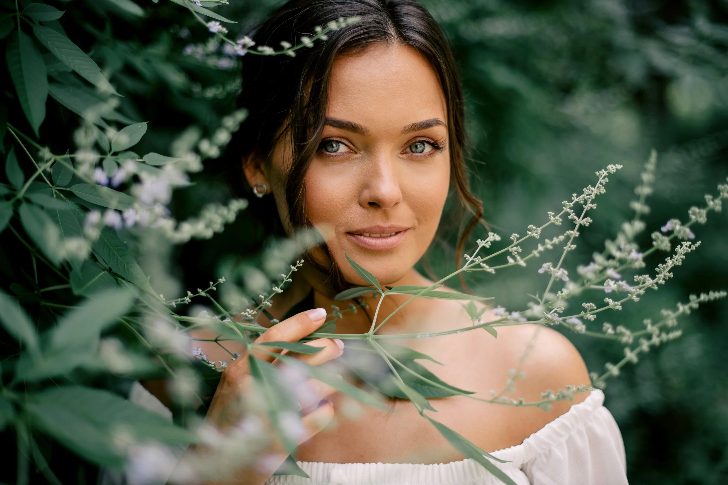 Una donna con capelli castani e occhi chiari tra foglie verdi e fiori bianchi