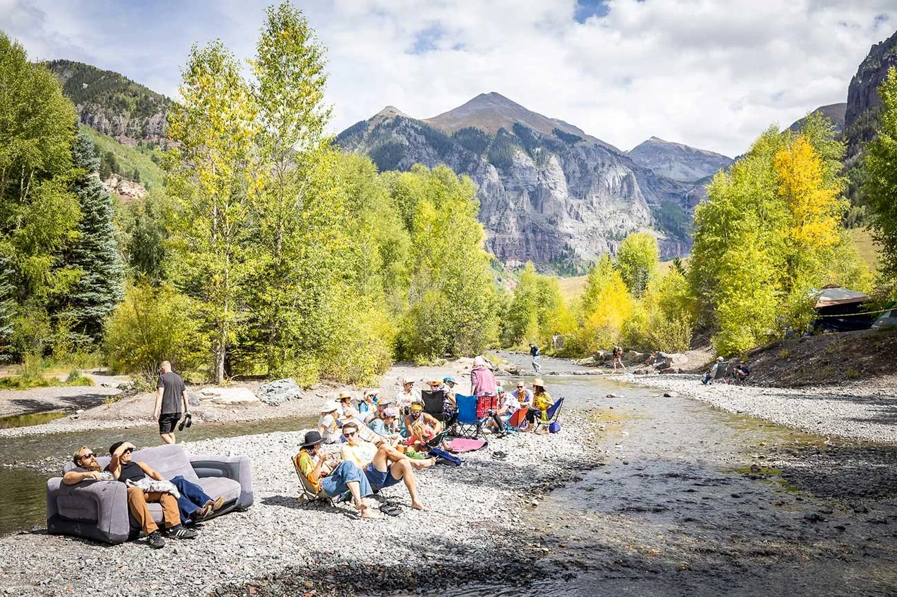 Festival attendees relaxing in chairs along the river, surrounded by the San Juan Mountains, capturing the adventurous spirit of Telluride Blues & Brews Festival.