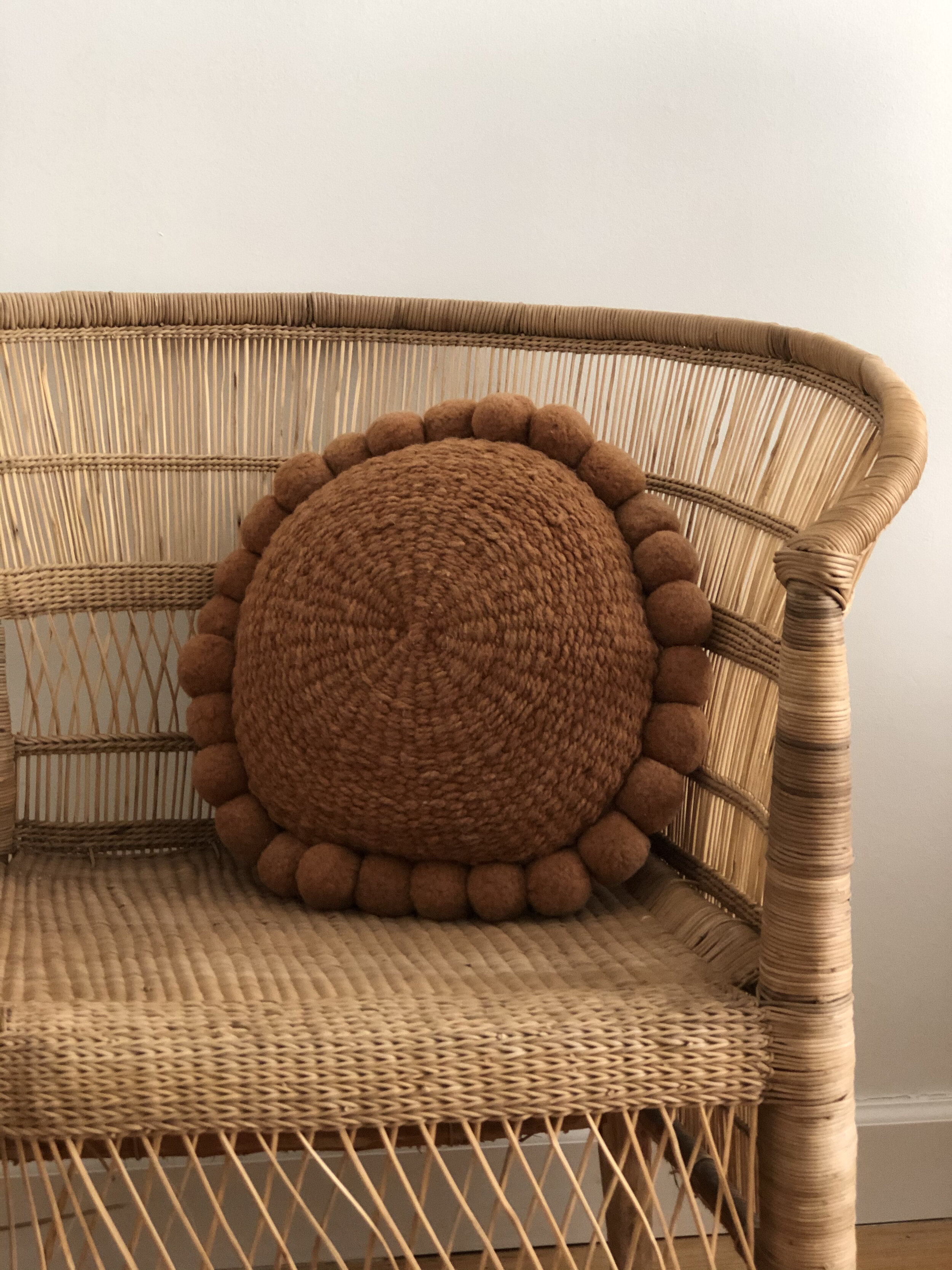 Rattan chair with round brown woven pillow featuring pom-pom edges.