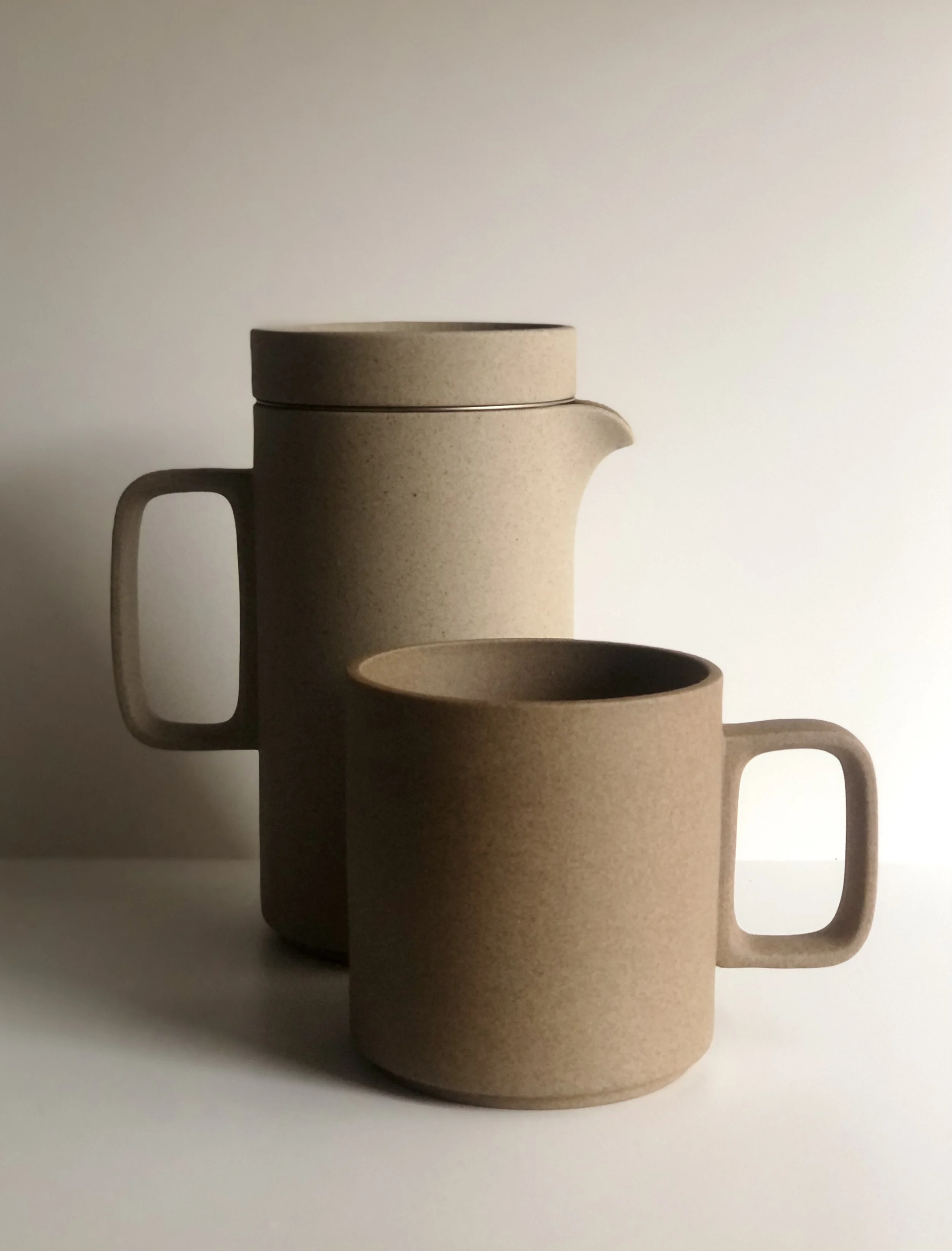 Minimalist beige ceramic mug and pot on white background
