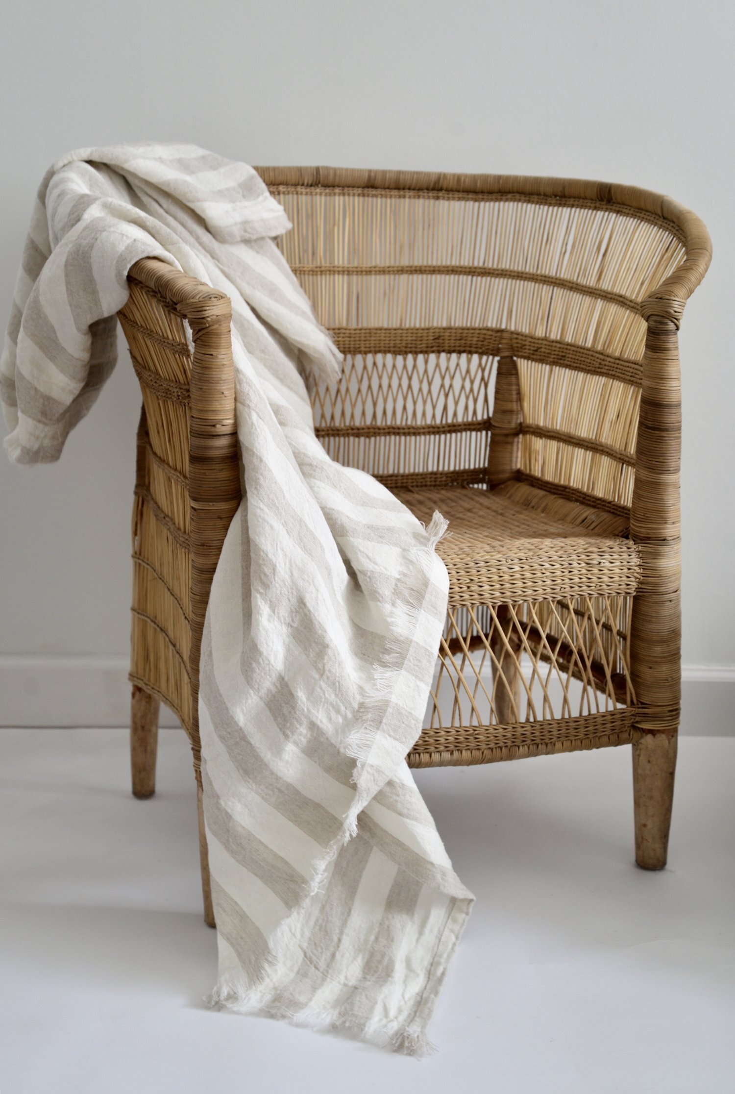 Wicker chair with a striped linen throw draped over it, against a light background.