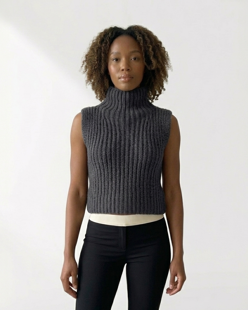 South African model wearing sleeveless sky grey chunky knit turtleneck vest with long beaded necklace and green tassel. High neck ribbed sweater showcases South African craftsmanship, Studio Minimale
