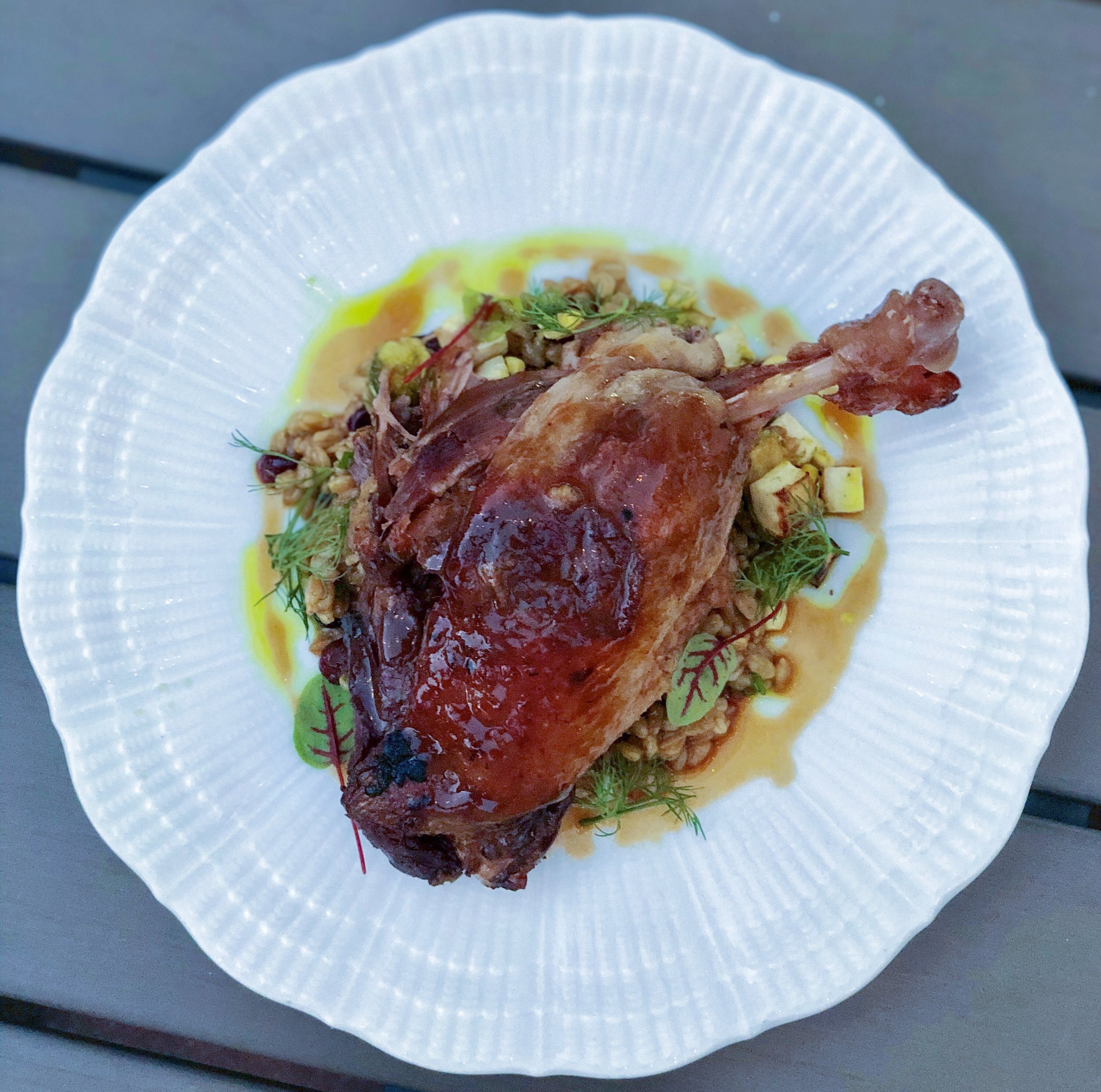 crispy roasted duck leg in yellow cream sauce on white plate