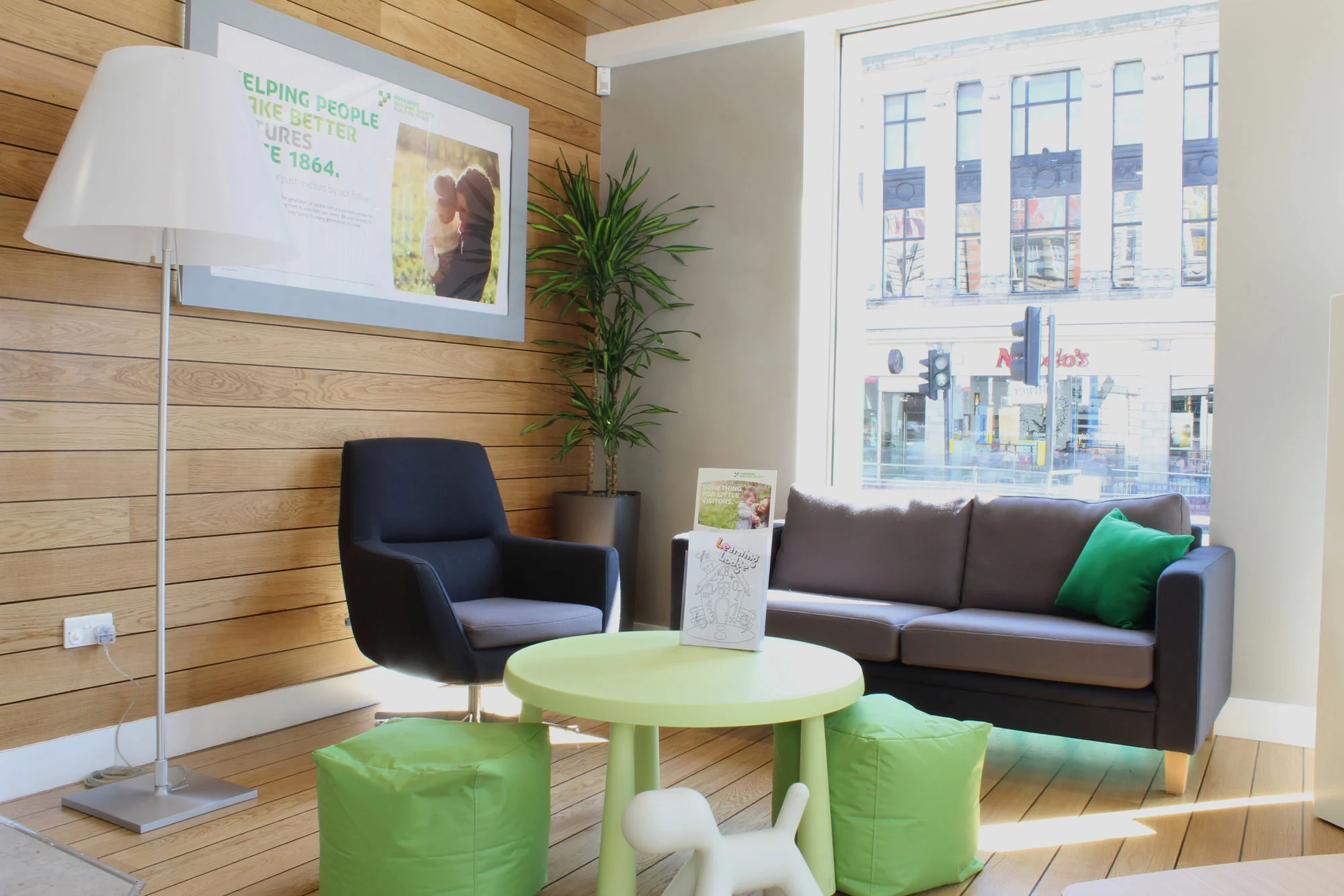 YBS waiting area with soft furnishings, green table, blue chair, grey sofa and large lamp