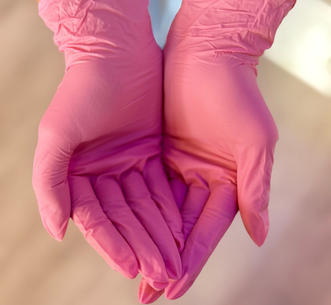 Two hands in pink gloves forming a heart shape with fingers
