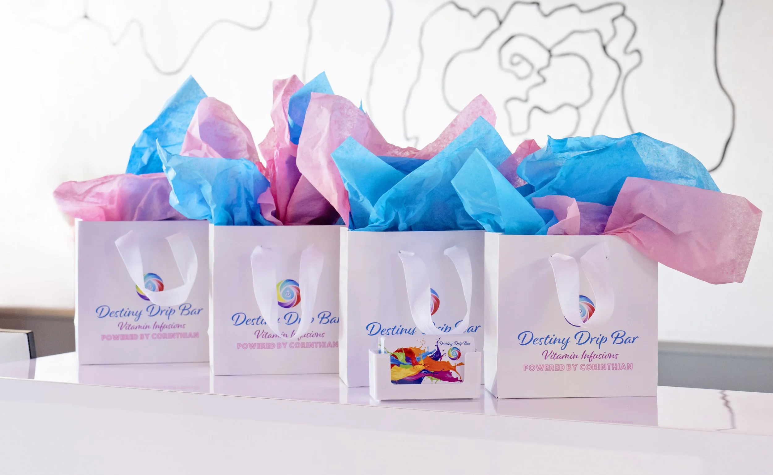 White boxes labeled 'Destiny Drip Bar' filled with pink and blue tissue paper, with a background featuring a simple black line drawing of a face.