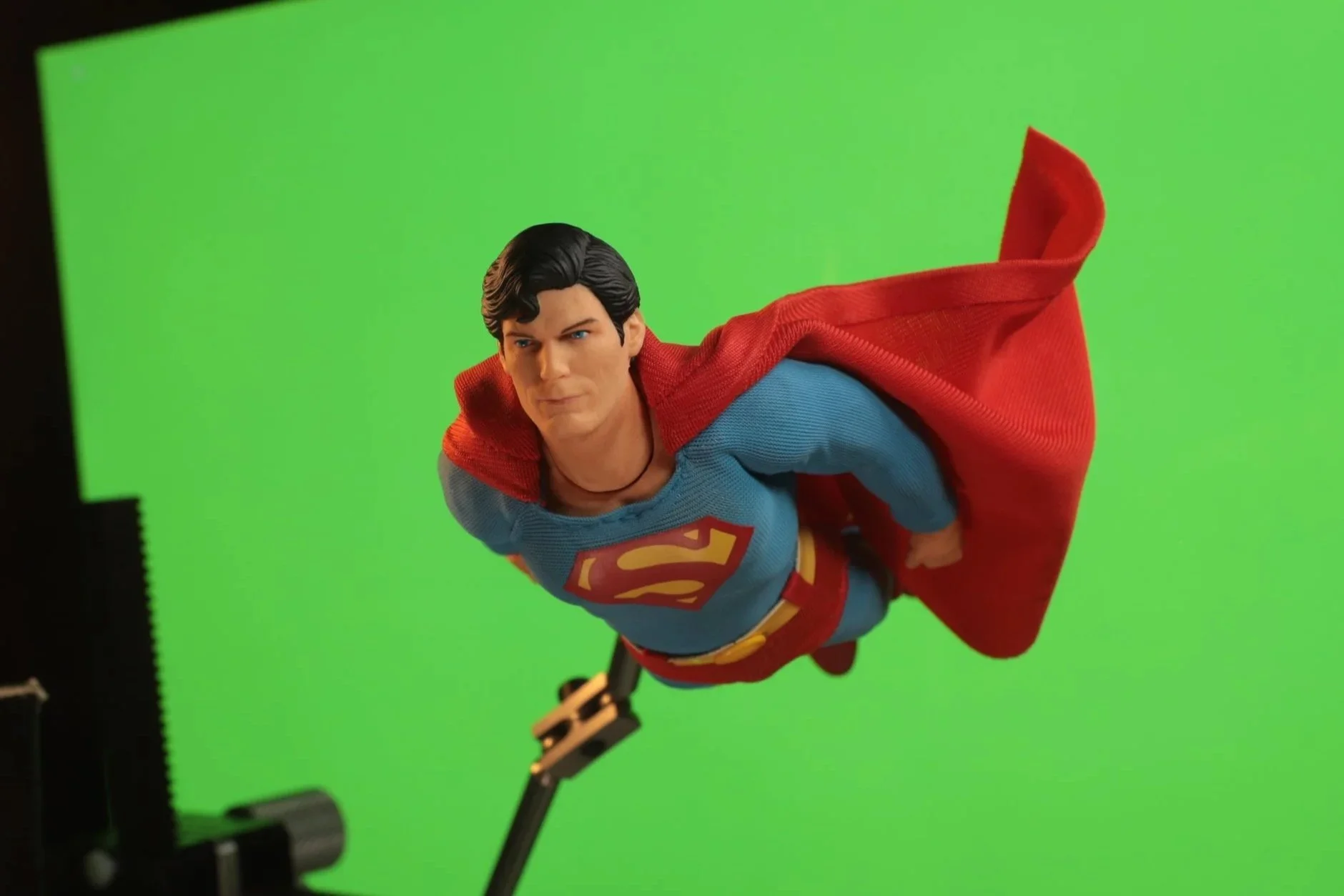 Superman action figure in flight pose with green screen background.