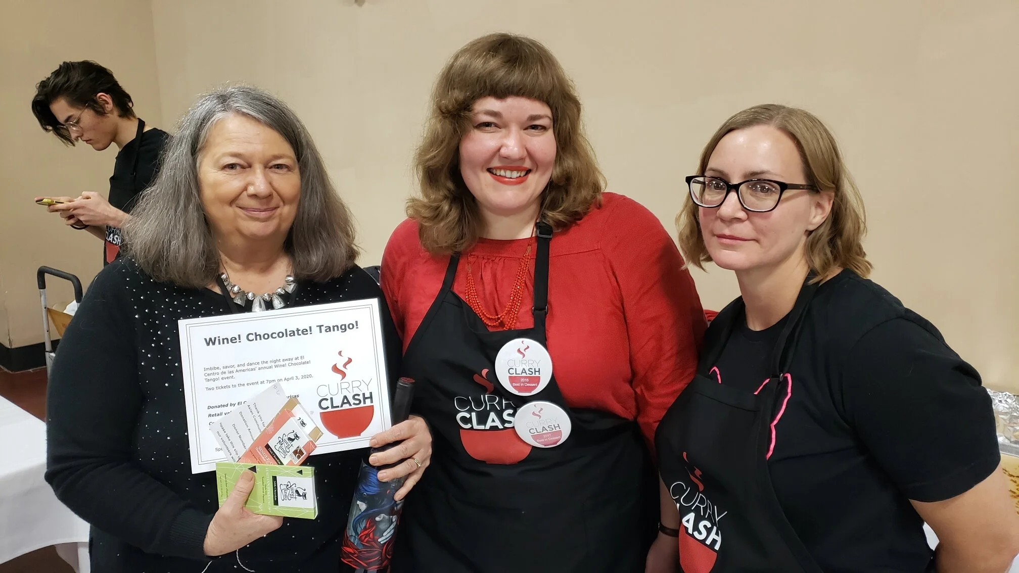 At the annual Curry Clash fundraiser for Lincoln’s Asian Community and Cultural Center. Three women stand together and smile at the camera. On the left, one is holding two Sweet Minou chocolate bars and a certificate.