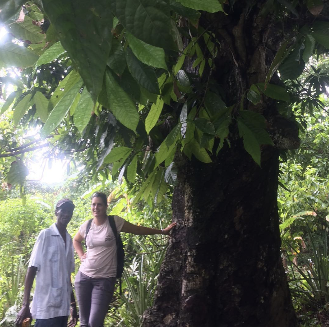  Farmer Bosier and manager Aline stand next to a cocoa tree and smile. 