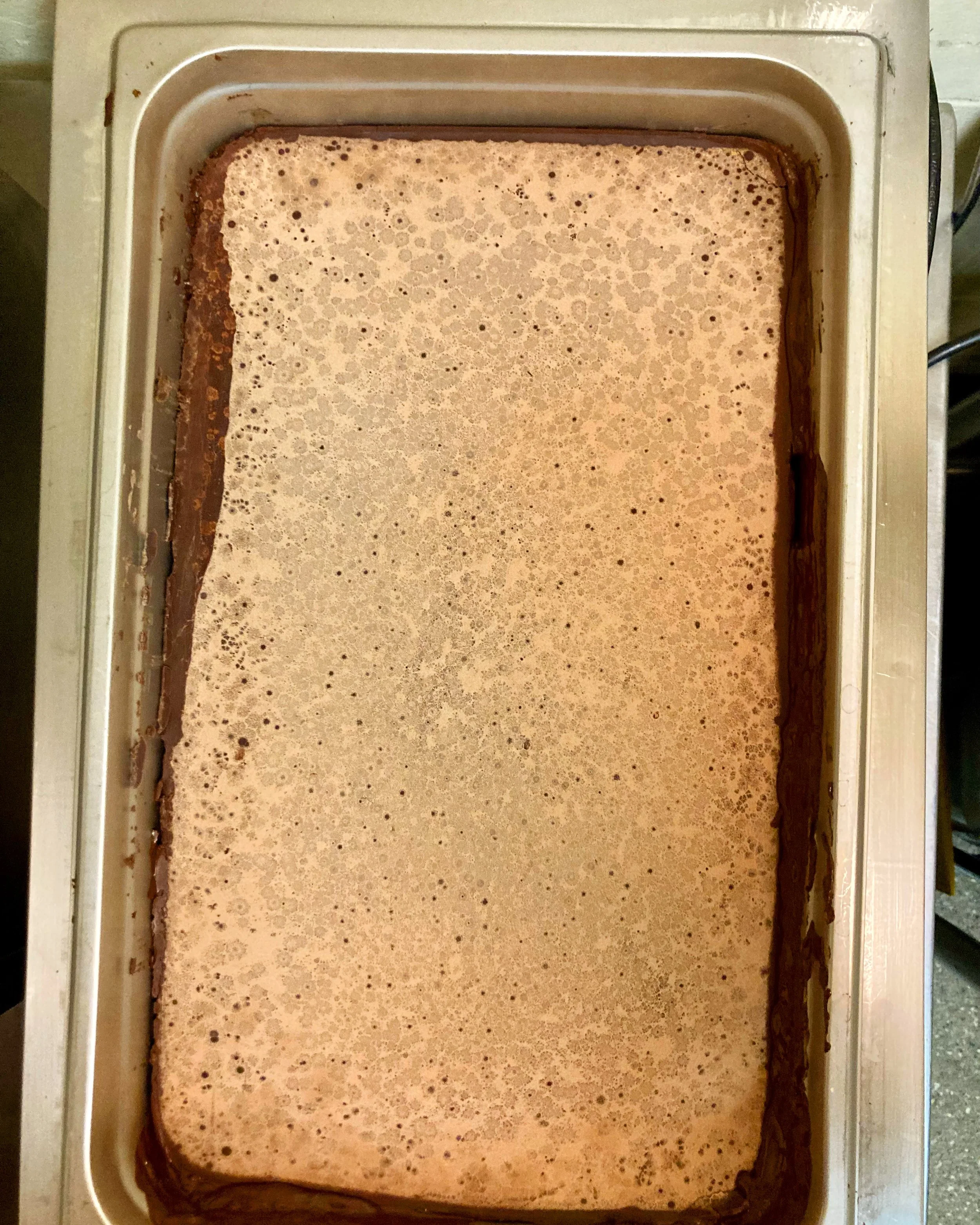  A pan of untempered chocolate melting. The fact that it is untempered makes the surface look dusty with varied crystalline patterns. 
