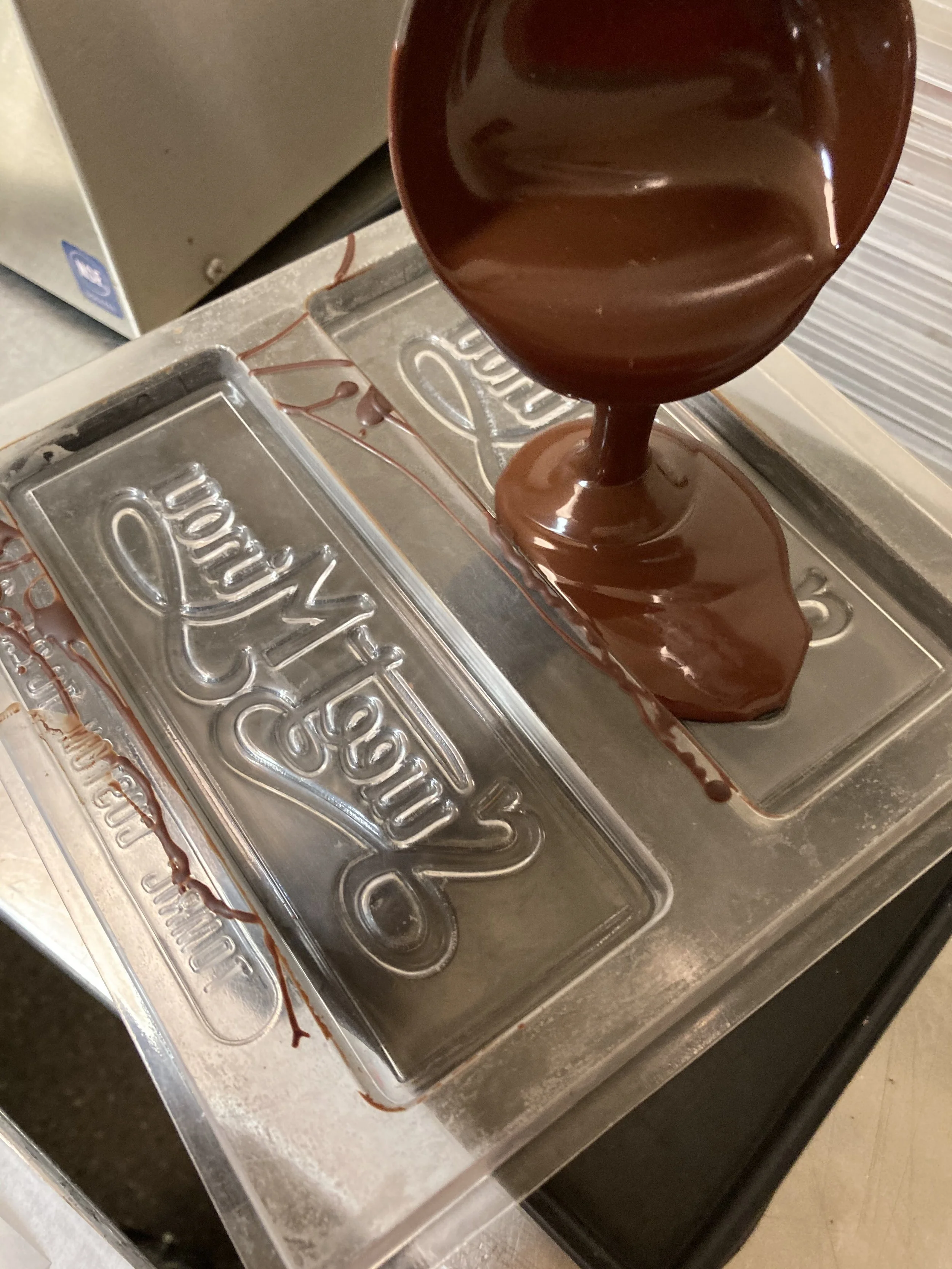  Melted, tempered chocolate being poured into a plastic Sweet Minou chocolate bar mold. Each bar is hand-poured. 