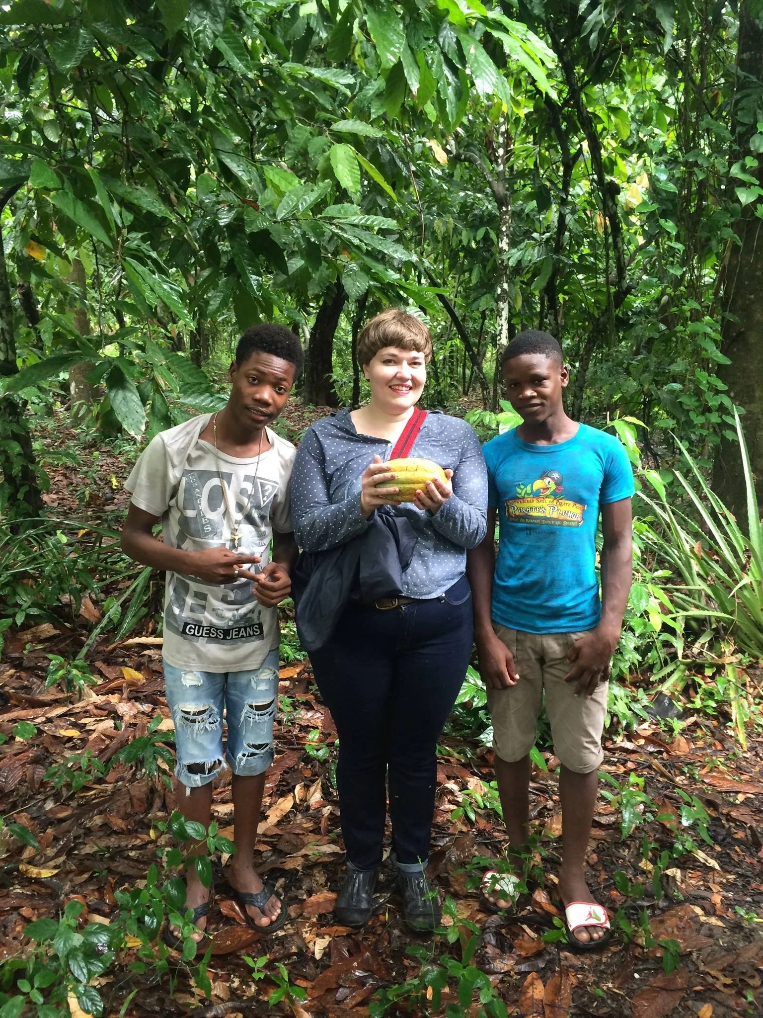  Rebecca stands with two of the teenage boys who live on cocoa farms in Northern Haiti. She is holding a yellow cocoa pod freshly harvested from a nearby tree. 