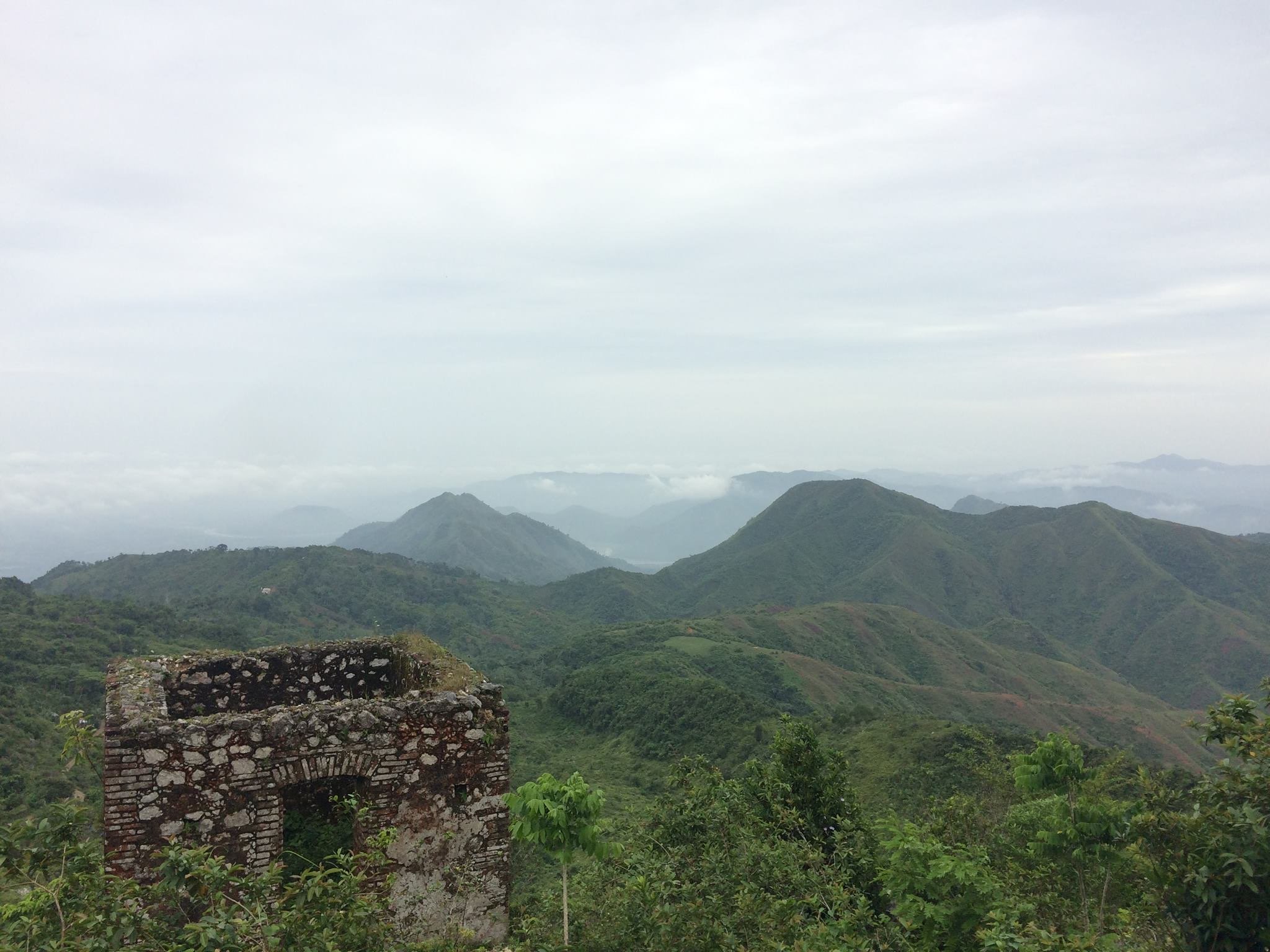  View of the northern Haitian countryside. There are many sloping hills covered in green, and fog hangs over the hills. 