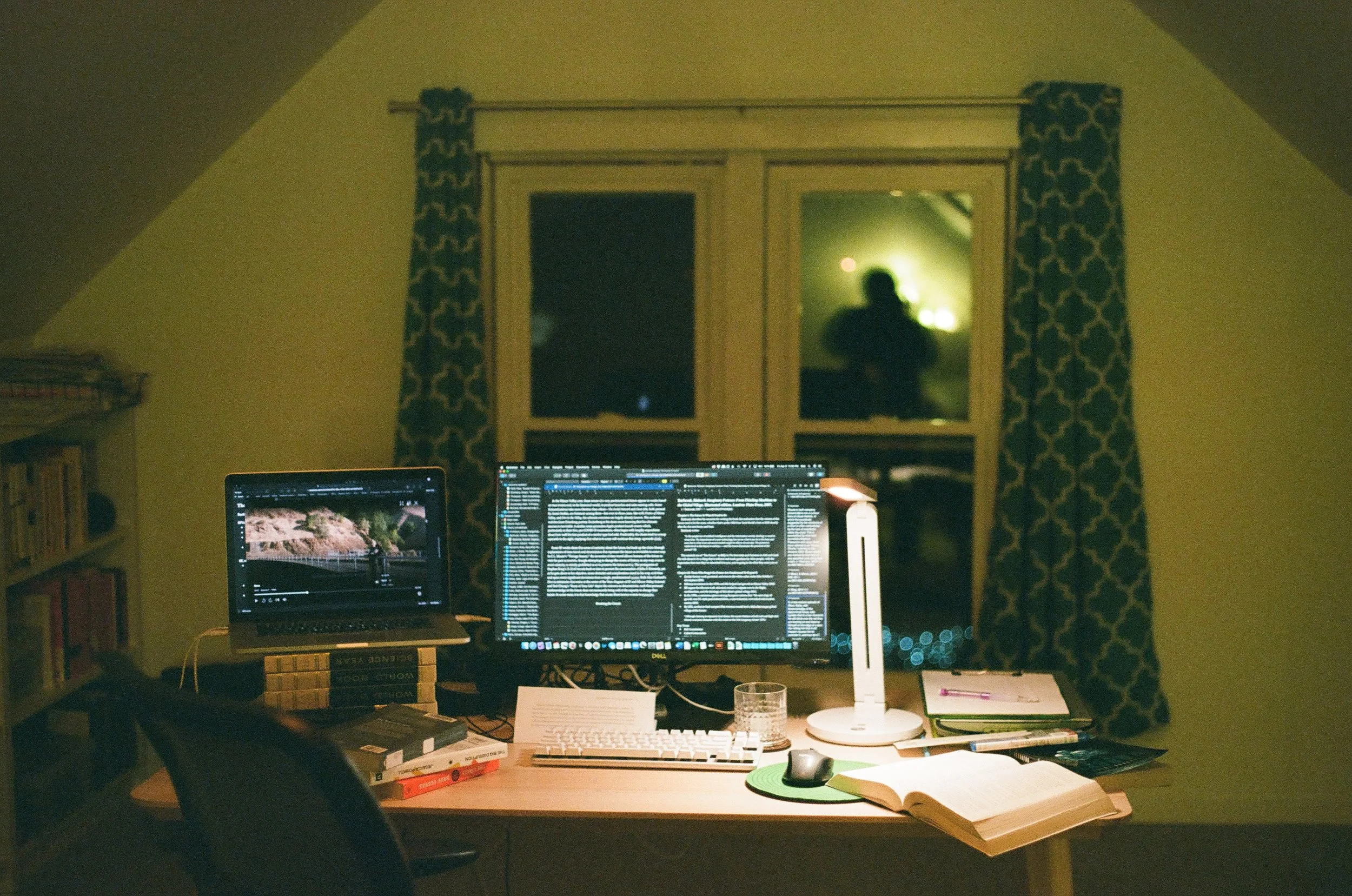 Desk with monitor, lamp, laptop, and books. Early AM.
