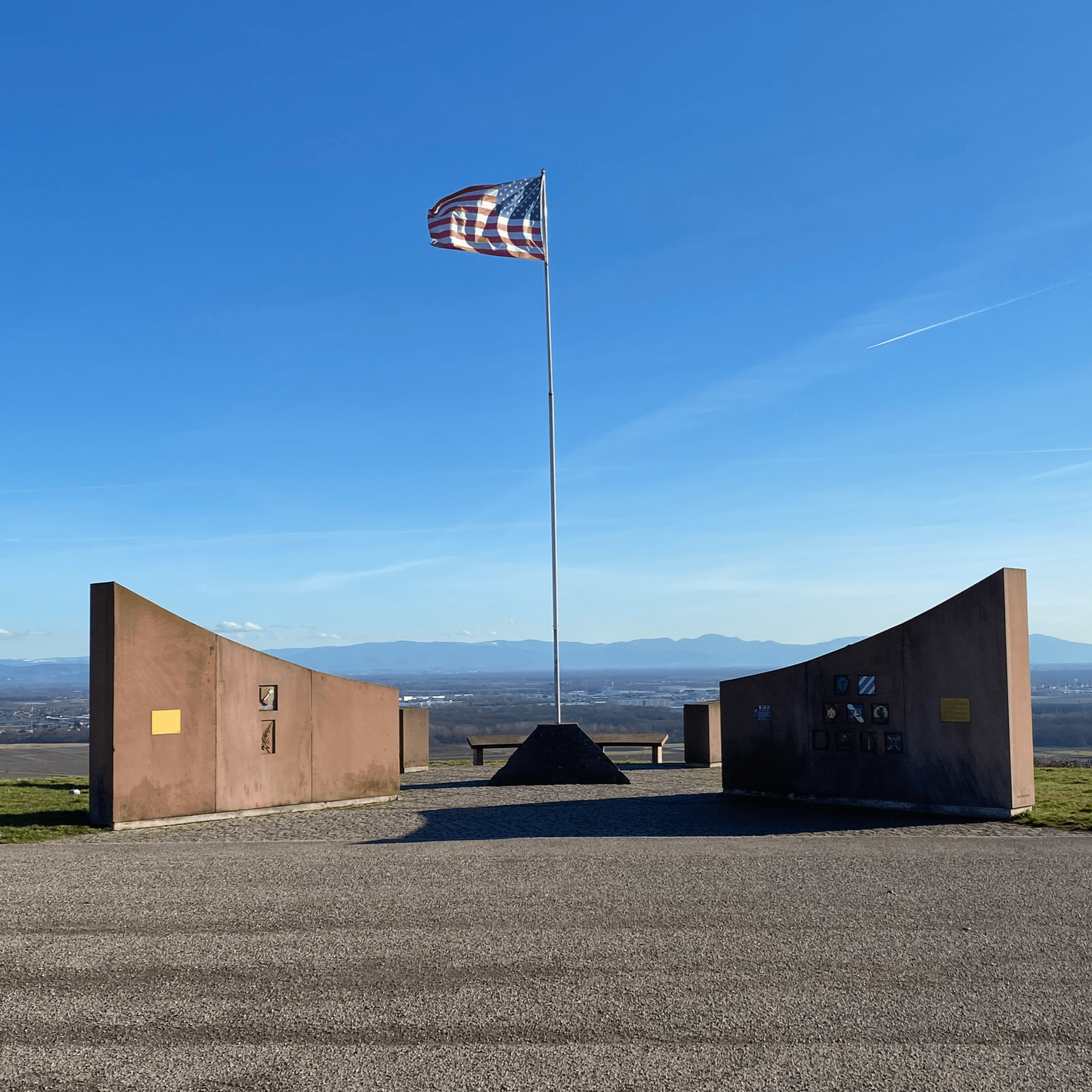 American memorial above Sigolsheim, US flag and unit-insignia walls overlooking the Colmar Pocket battlefield and the Vosges.