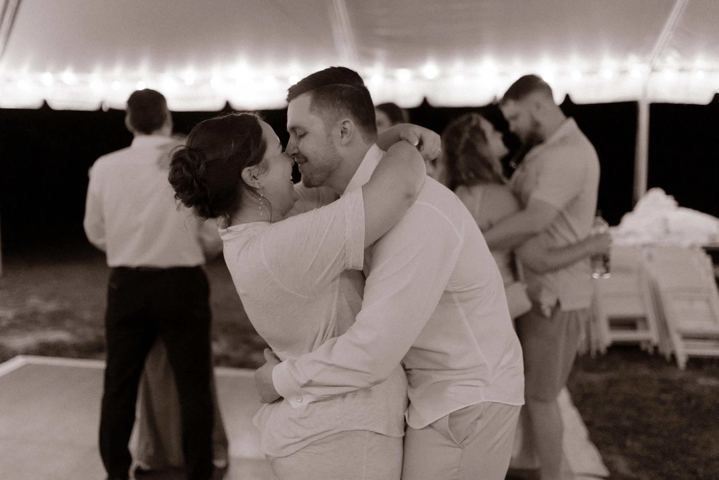 Newlyweds slow dancing under twinkle lights in comfy clothes during the final night of their wedding weekend.