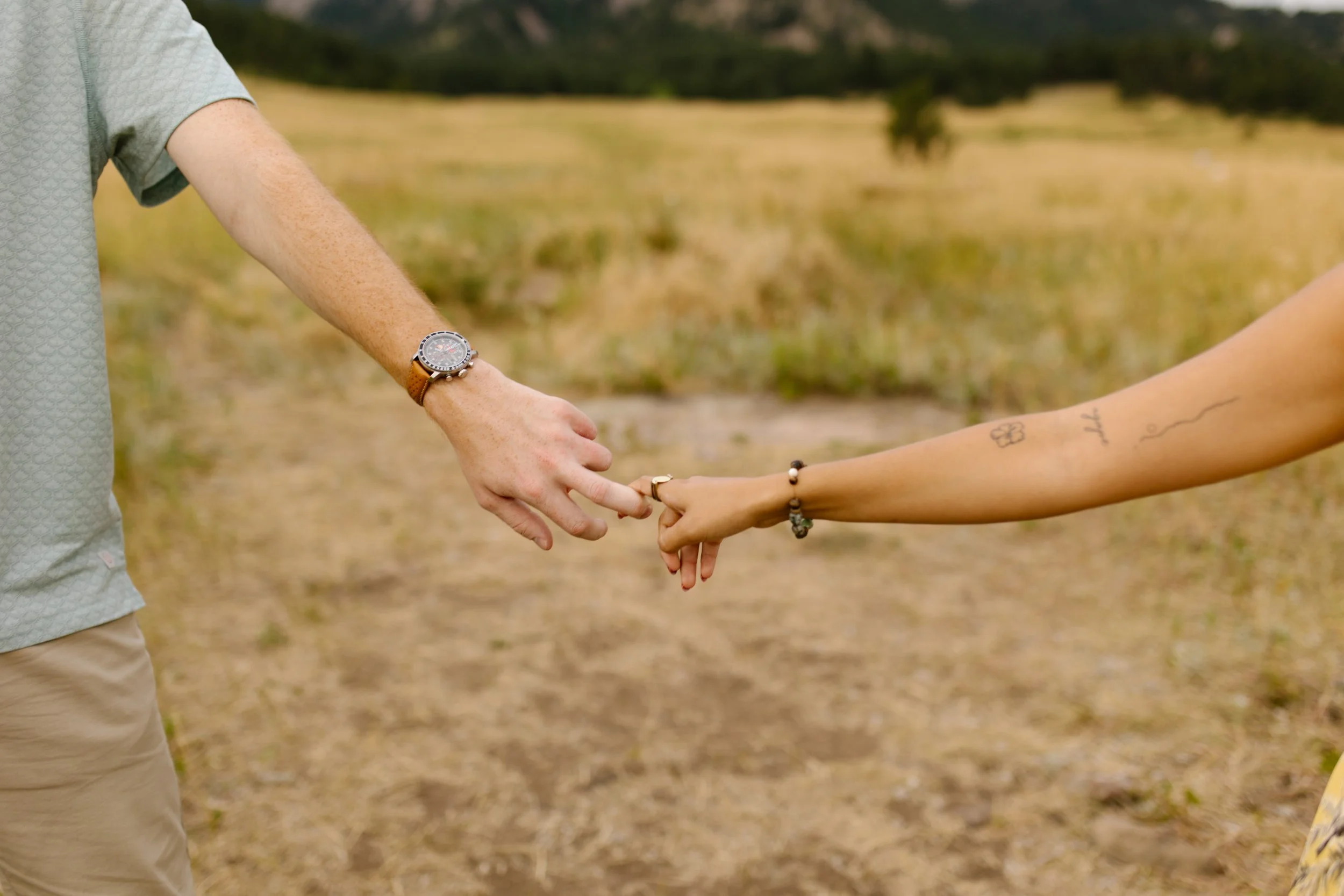 Close-up of newly engaged couple’s hands reaching toward each other, showing off her ring after the proposal.