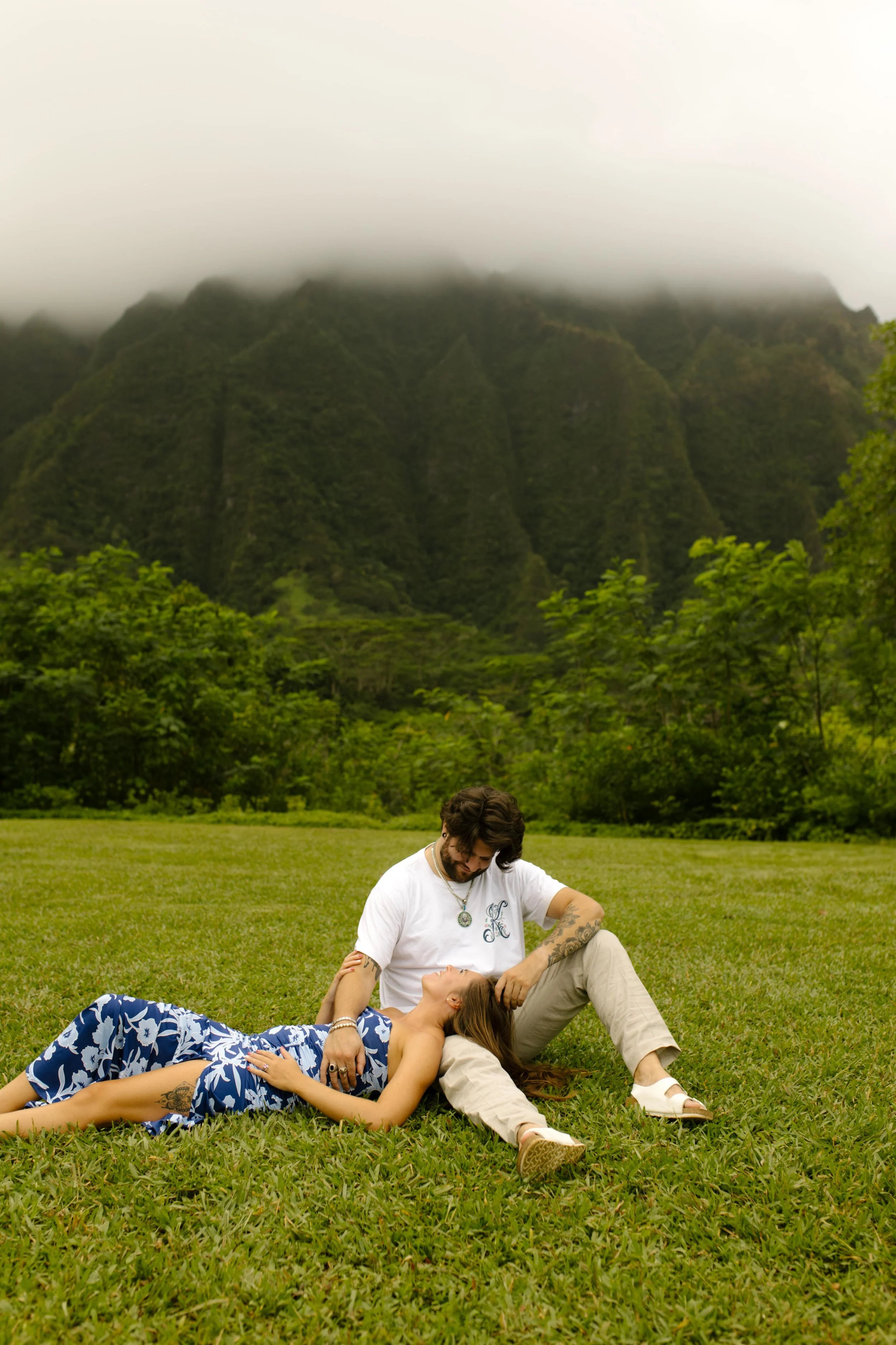 Woman rests head on fiance's lap while sitting on grassy field together