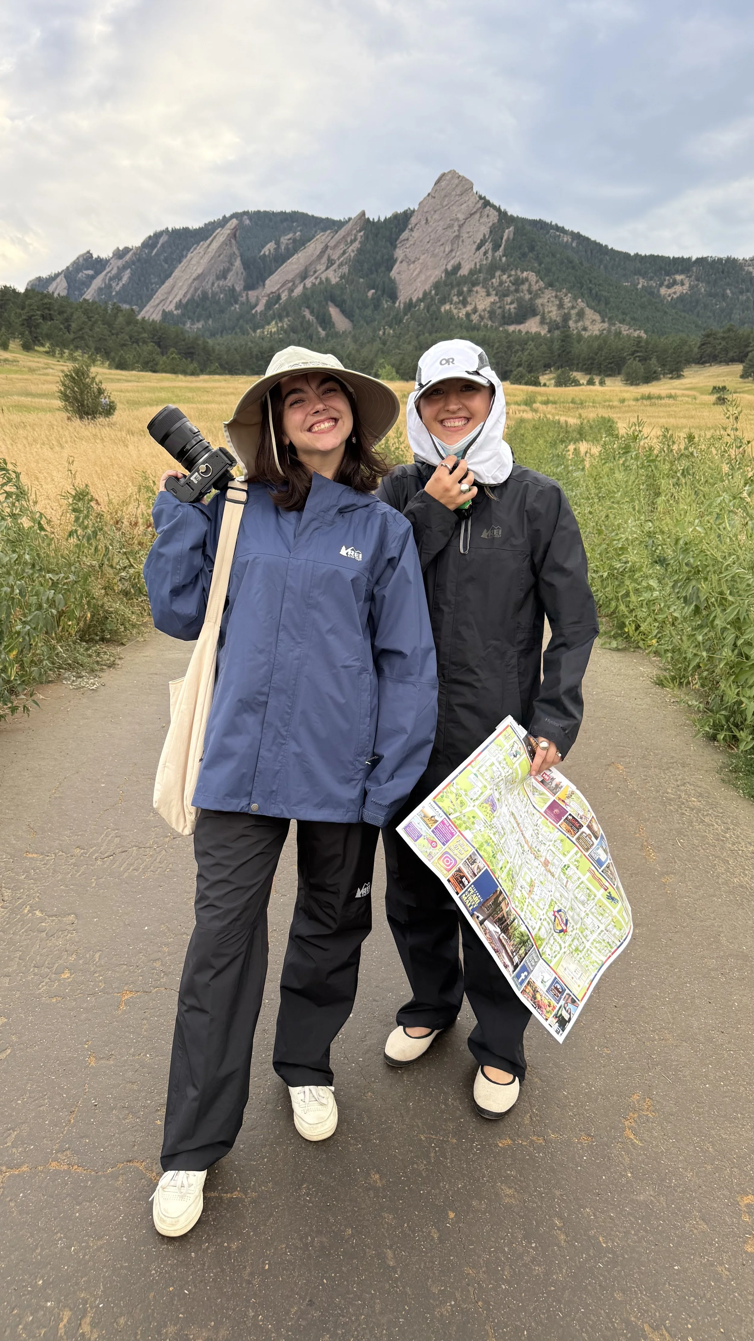 Two friends dressed in hiking gear holding a camera and map while scouting the Flatirons for a surprise engagement shoot.
