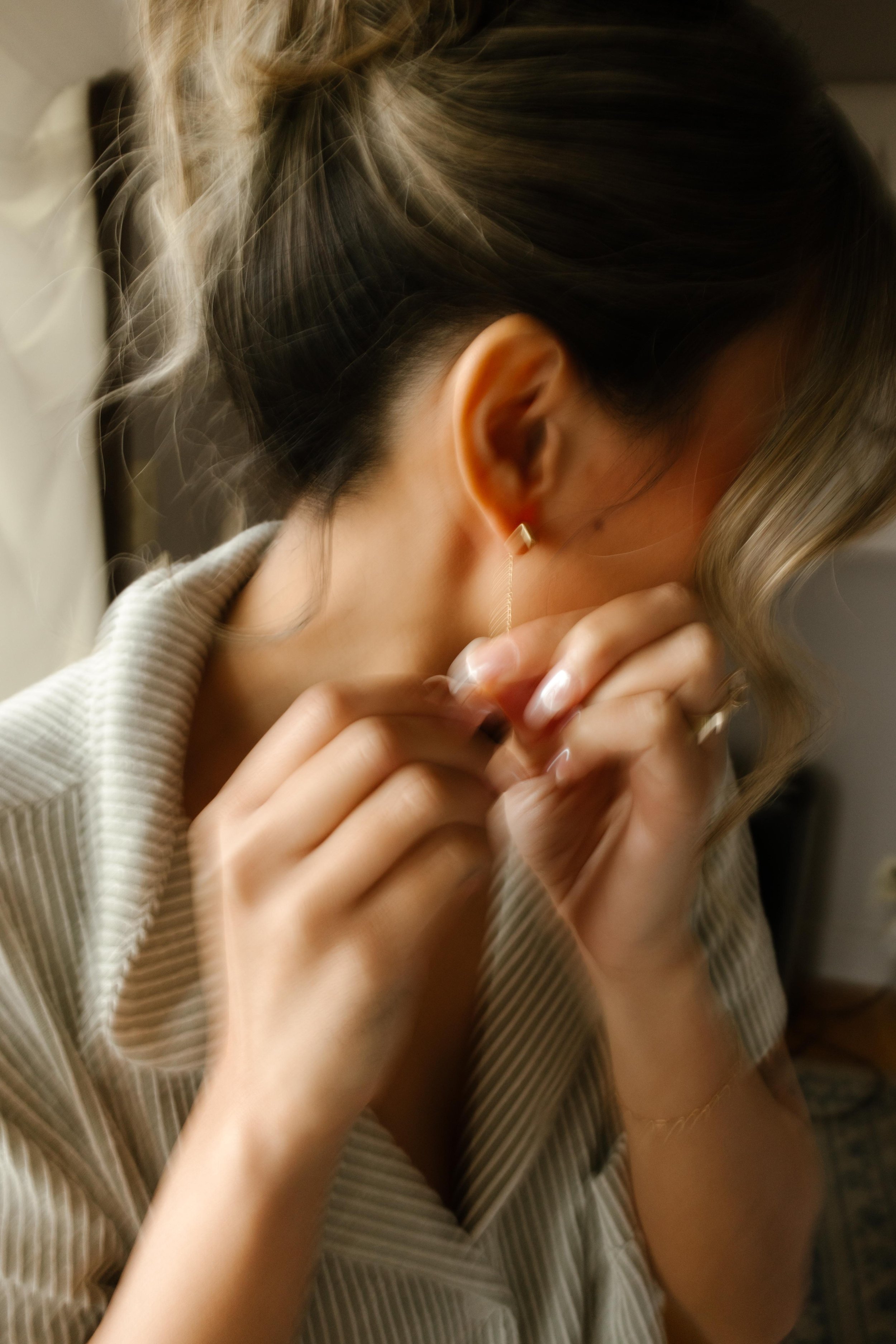 A blurred close-up of the bride putting on her earrings, soft curls framing her face as she gets ready.