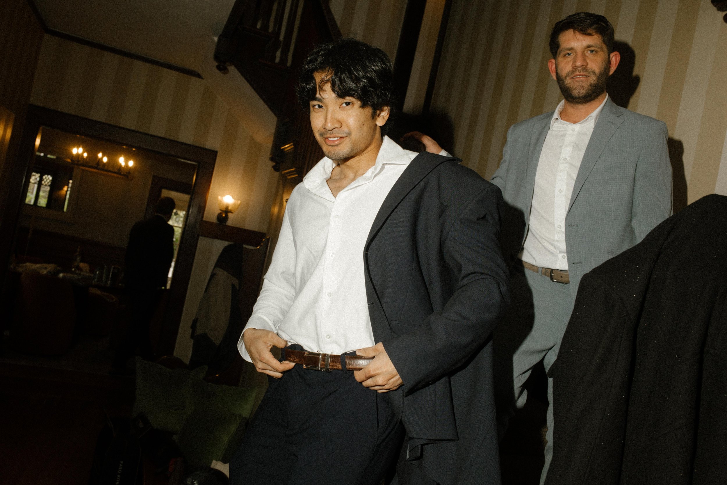 Groomsmen getting ready in a dimly lit room, adjusting suits and sharing quiet pre-ceremony energy.