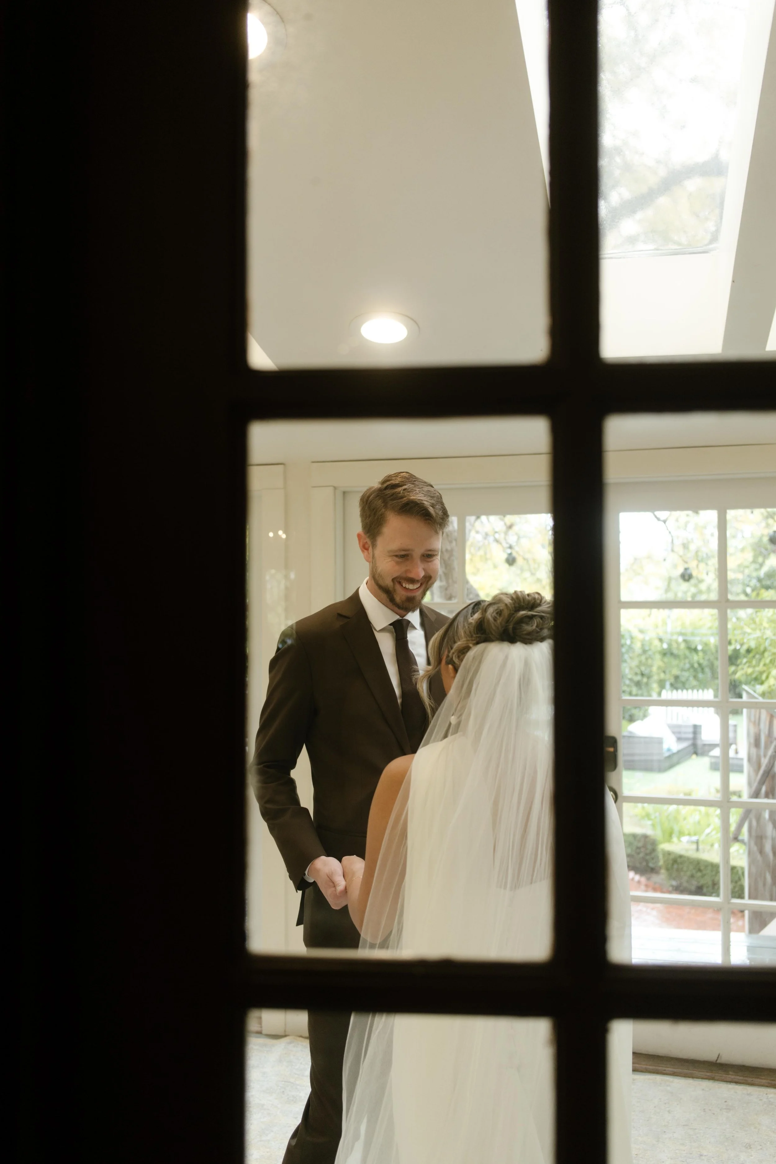 A behind-the-door view of the groom smiling as he sees his bride during their first look on the morning of their wedding.