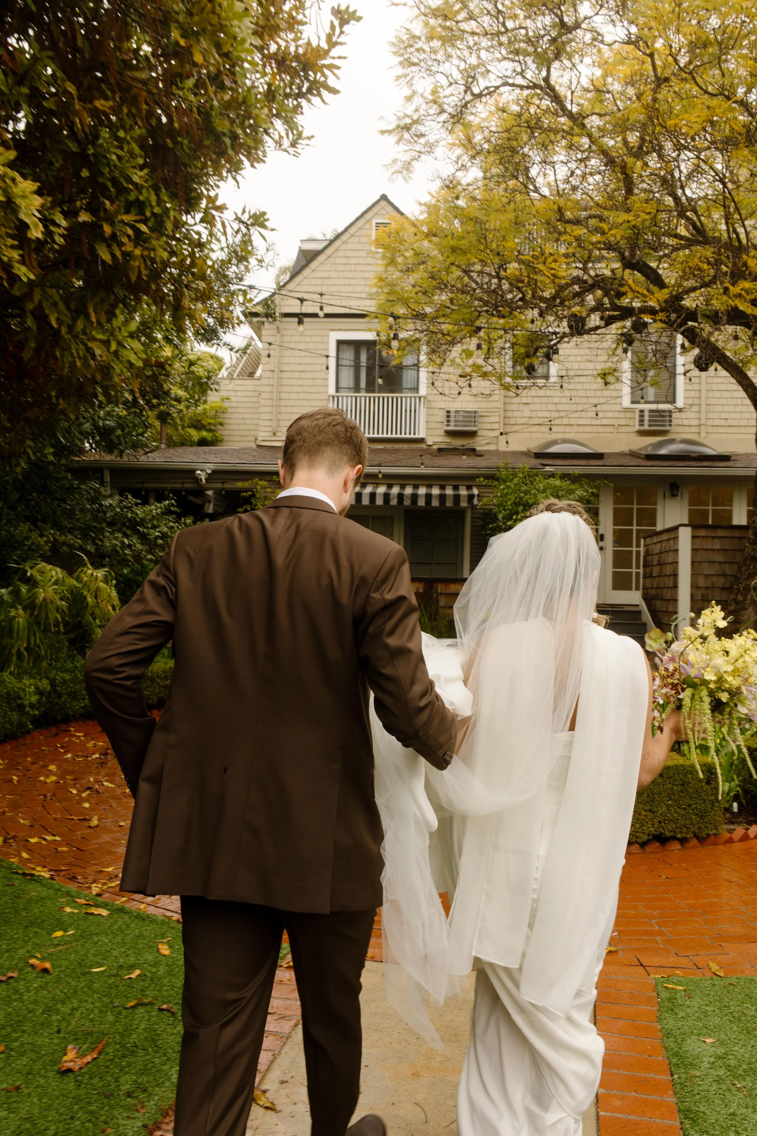 The couple walks hand in hand through a garden path, the bride’s train trailing behind as they head toward forever.