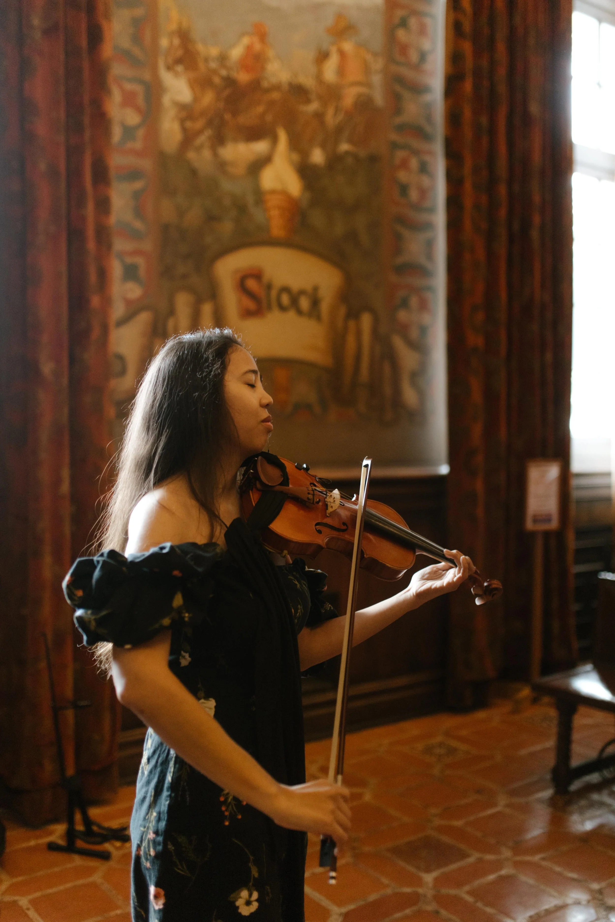 A violinist performs in the mural room during the wedding Santa Barbara Courthouse ceremony, surrounded by rich colors and history.