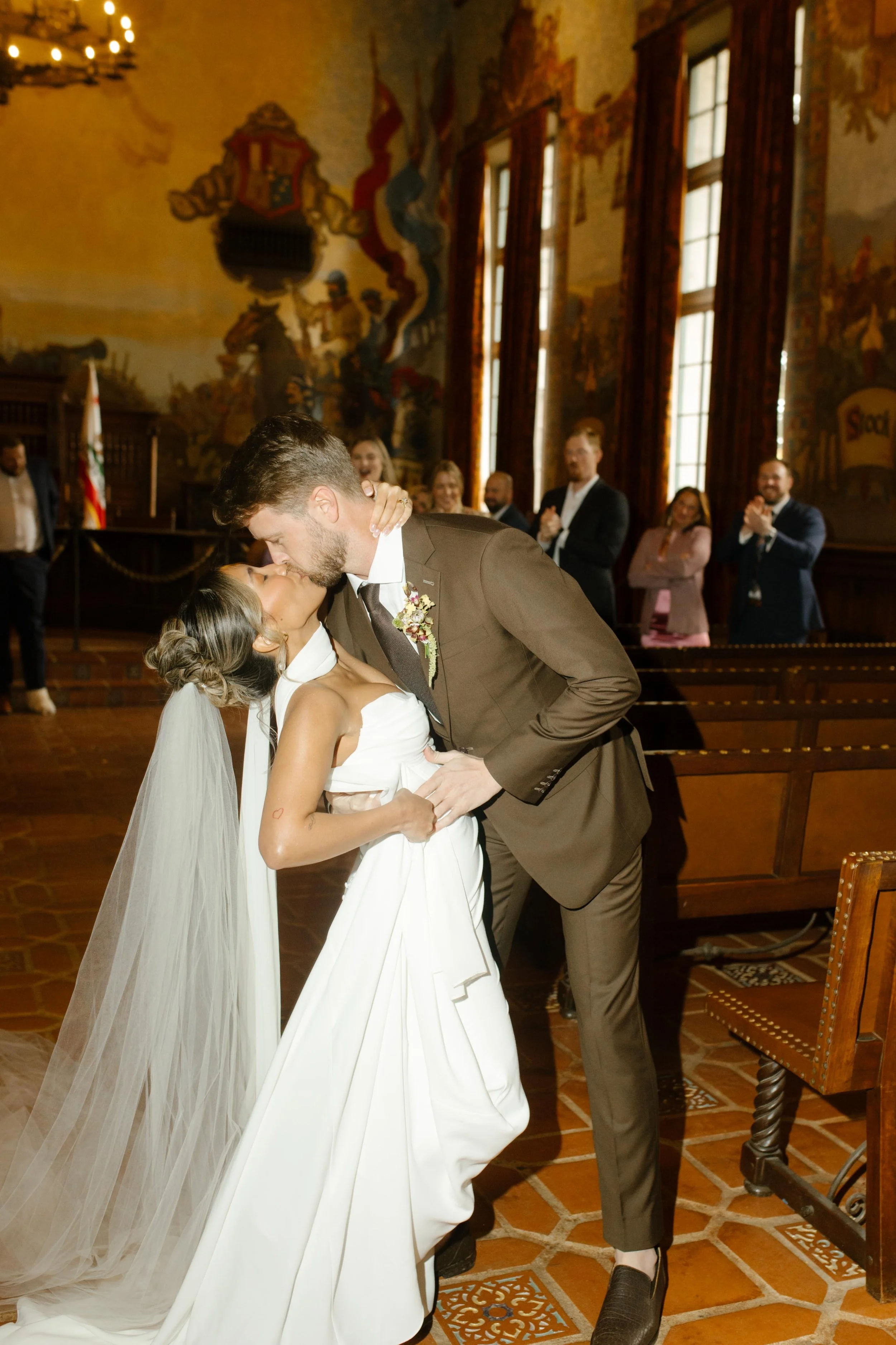 The couple shares a dip-kiss moment at the end of the aisle, surrounded by applause during their Santa Barbara Courthouse wedding.