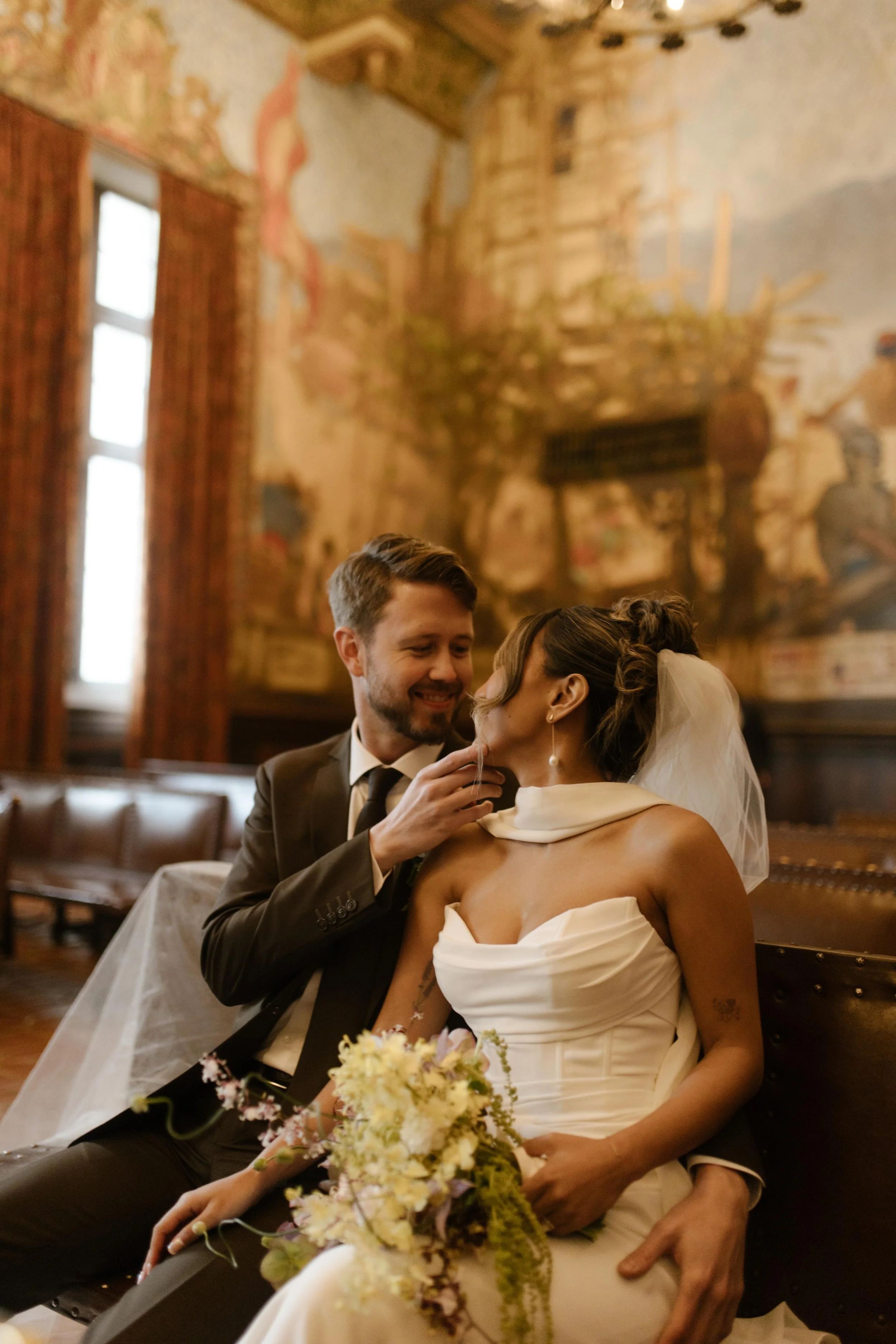 The newlyweds cozy up on a bench inside the mural room—romance rooted in wedding Santa Barbara Courthouse charm.