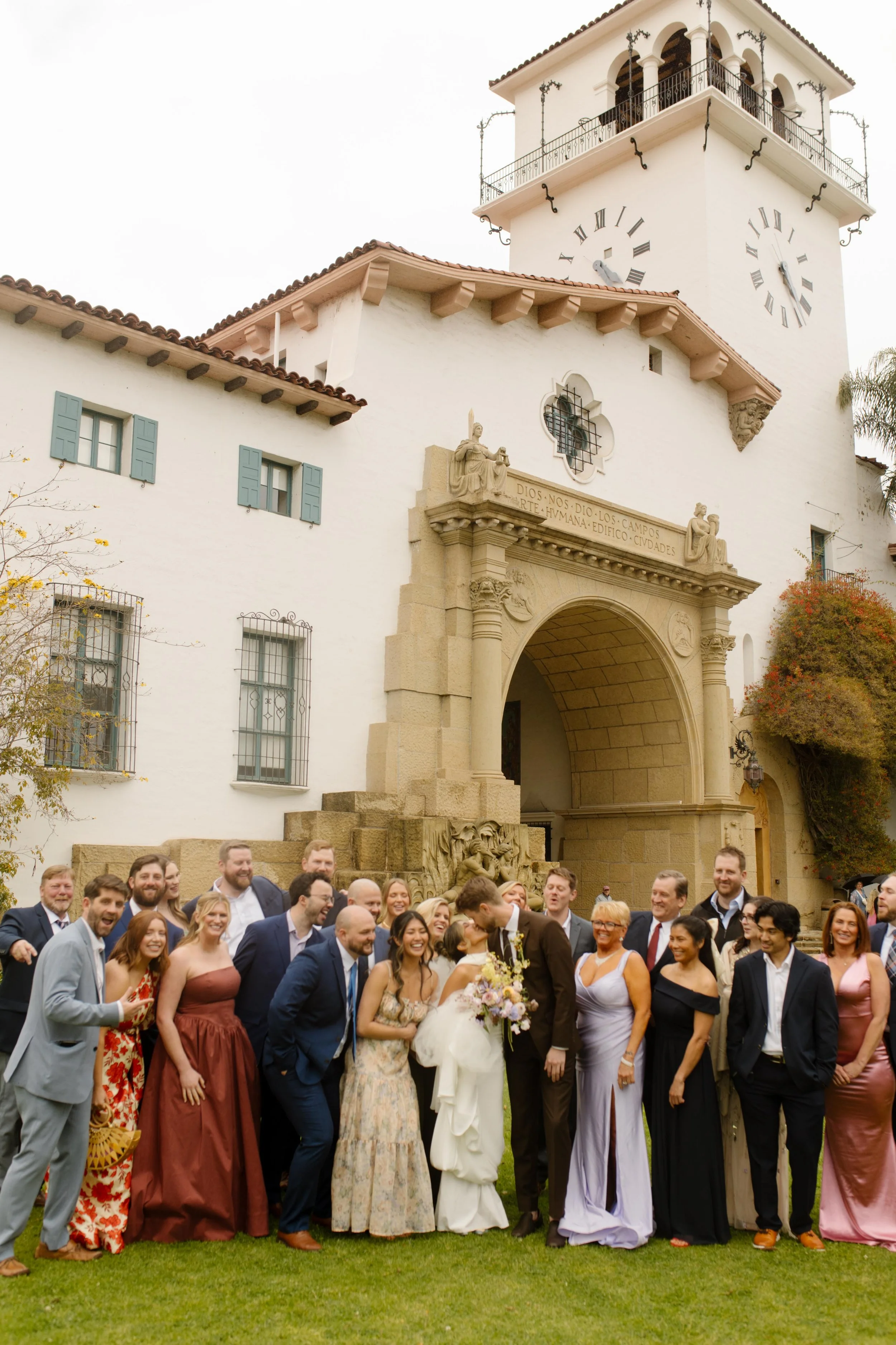 A full wedding party stands in front of the courthouse arch, all smiles and champagne energy.