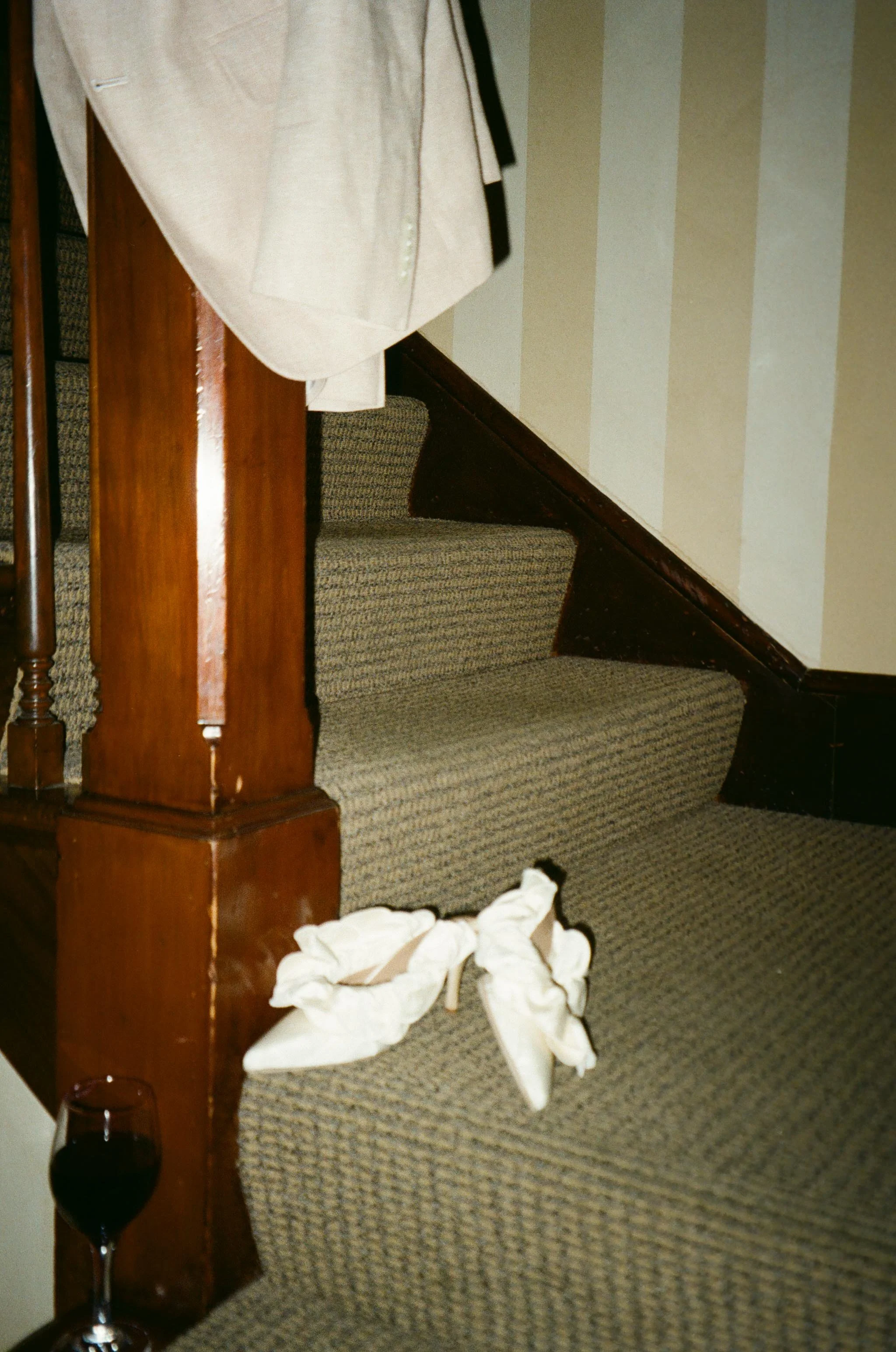 A pair of white heels and a jacket left at the base of a staircase.