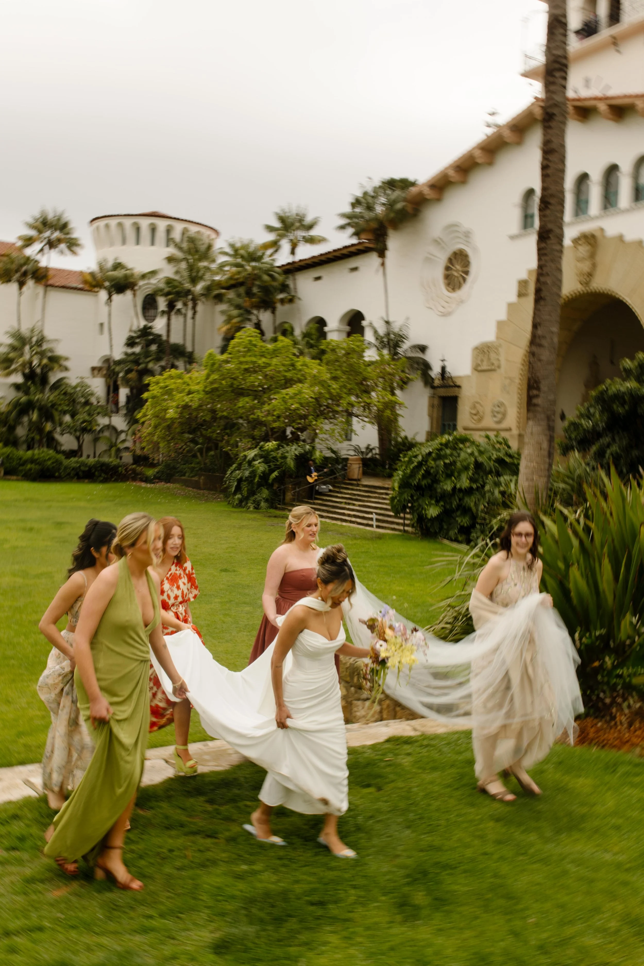 Bridesmaids assist with the bride’s train on the lawn during their wedding Santa Barbara Courthouse.