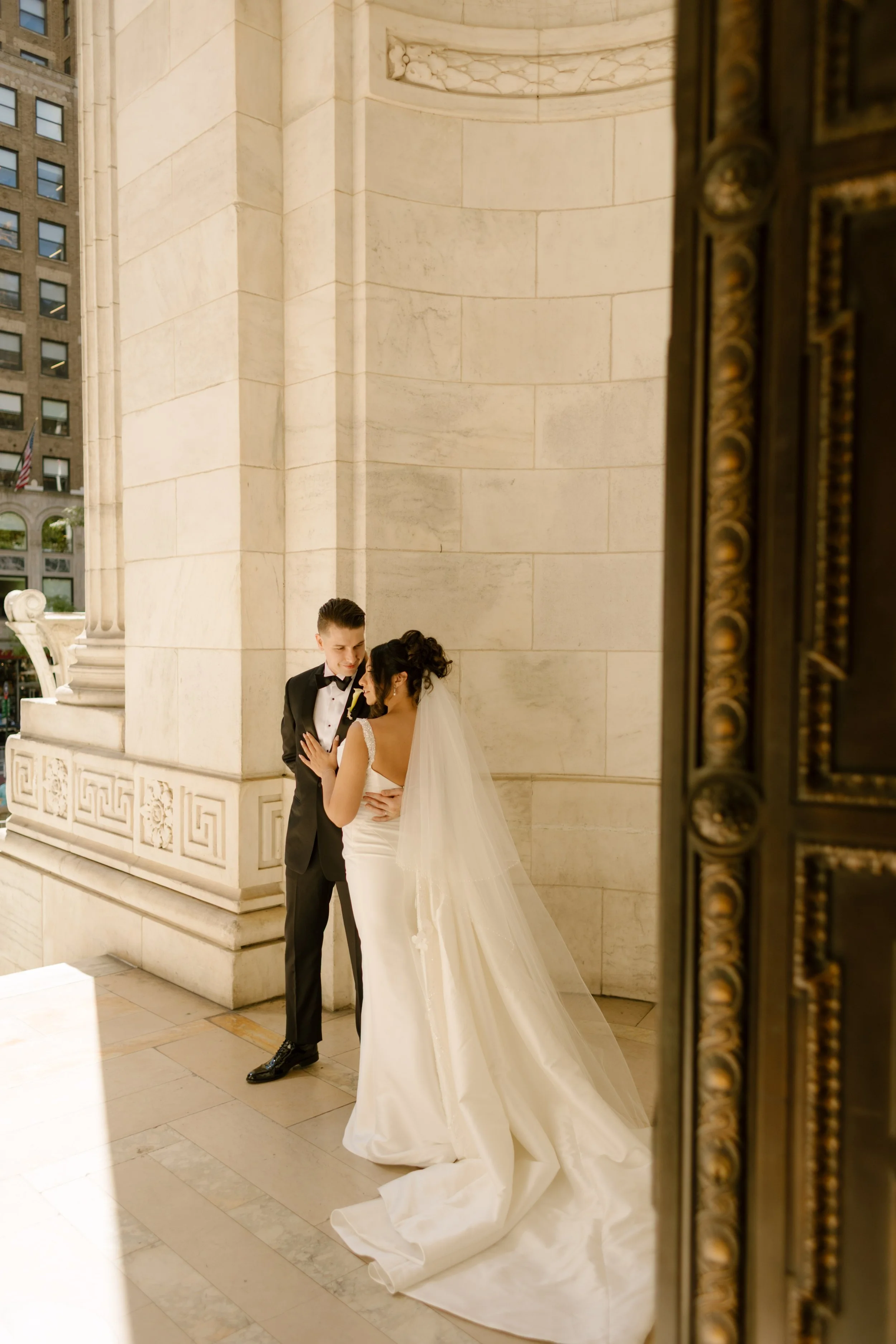 Bride and groom tucked into a quiet marble alcove of the New York Public Library, sharing a soft, intimate moment during their wedding in New York City.