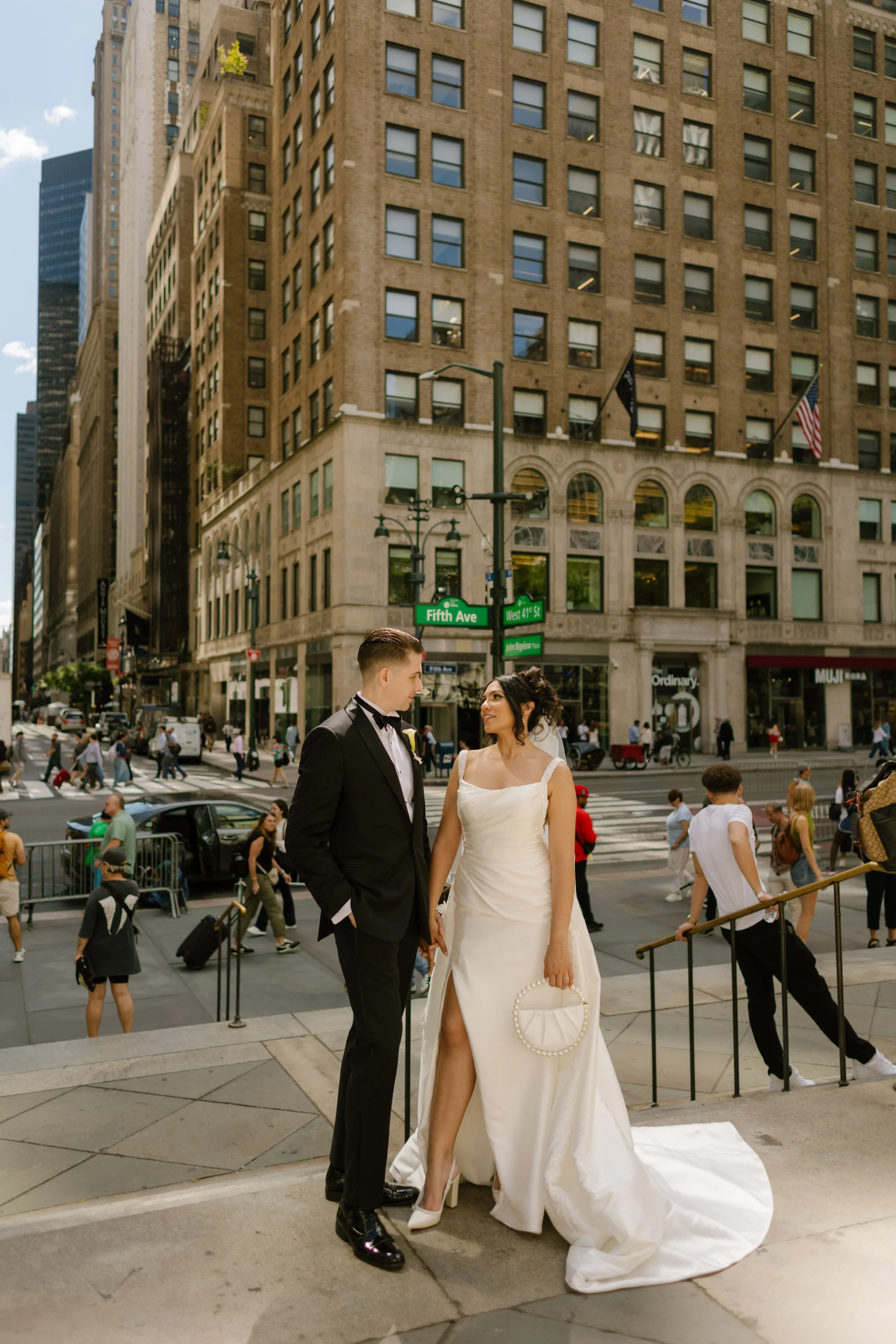 Bride and groom holding hands on the steps of Fifth Avenue, wrapped in each other amid the buzz of Midtown—a modern, romantic wedding moment in New York City.
