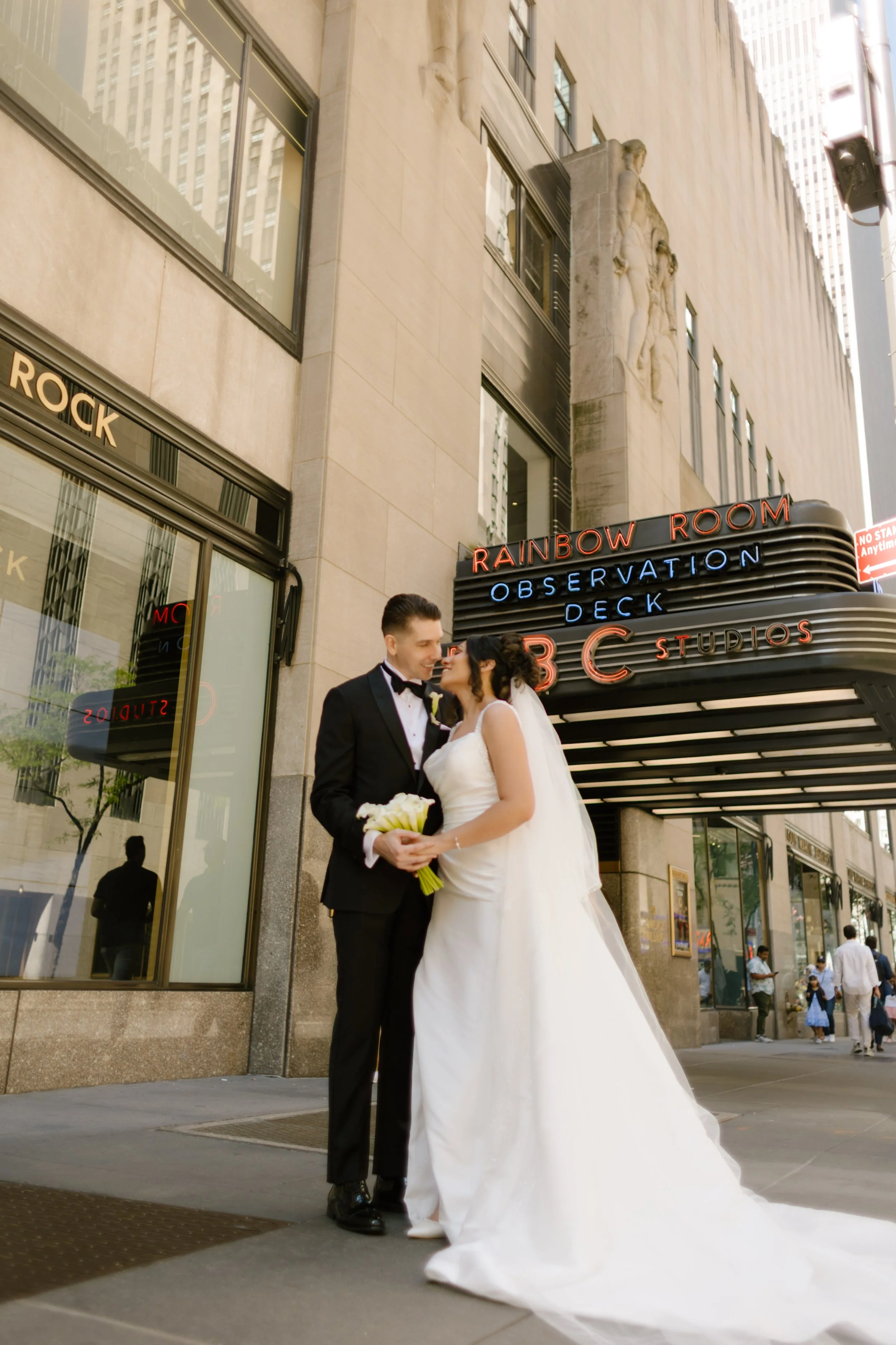 Bride and groom sharing a sweet moment outside the Rainbow Room and NBC Studios marquee—an iconic midtown stop during their wedding in New York City.