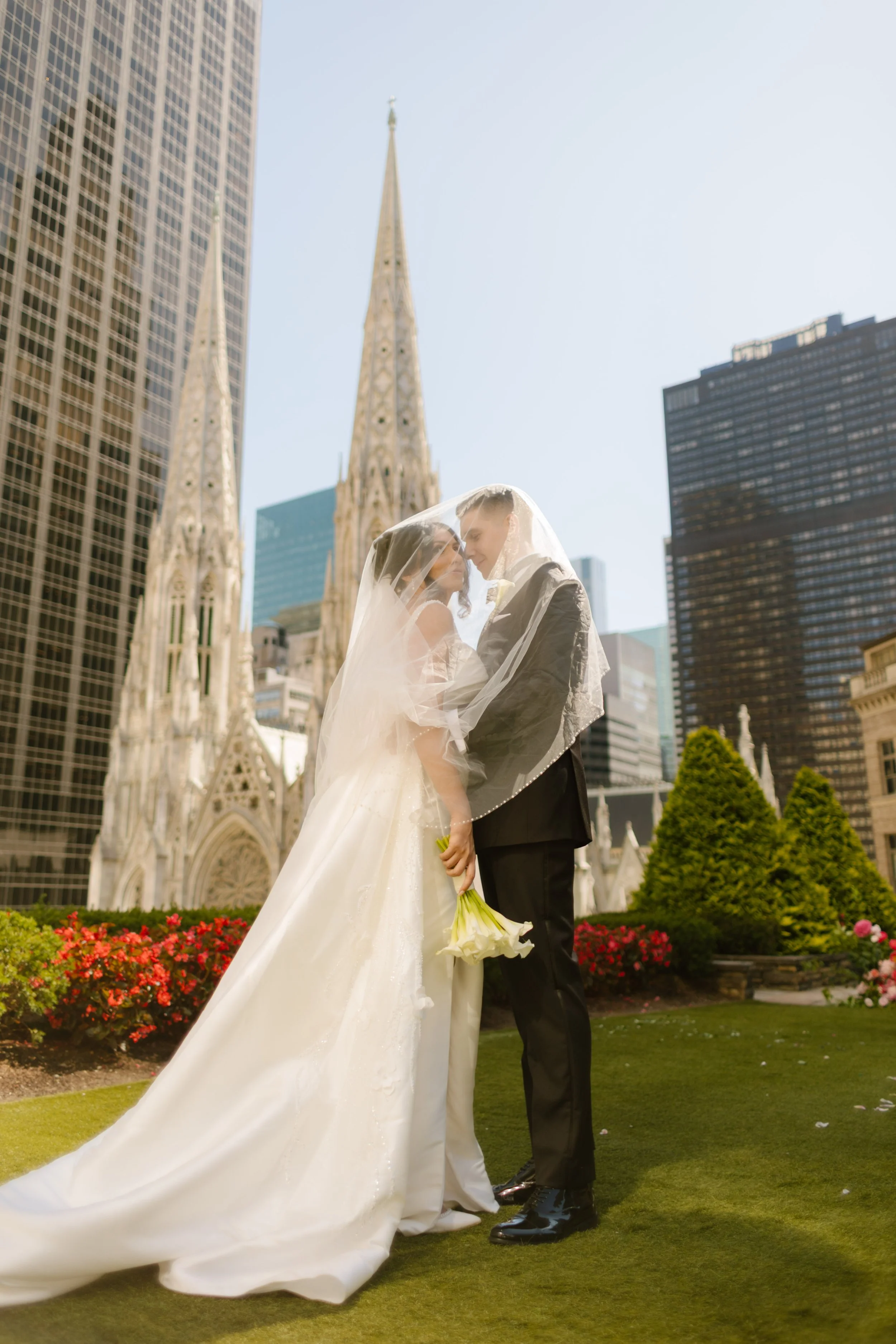 The bride and groom wrapped in her veil, forehead to forehead as skyscrapers and cathedral spires surround them
