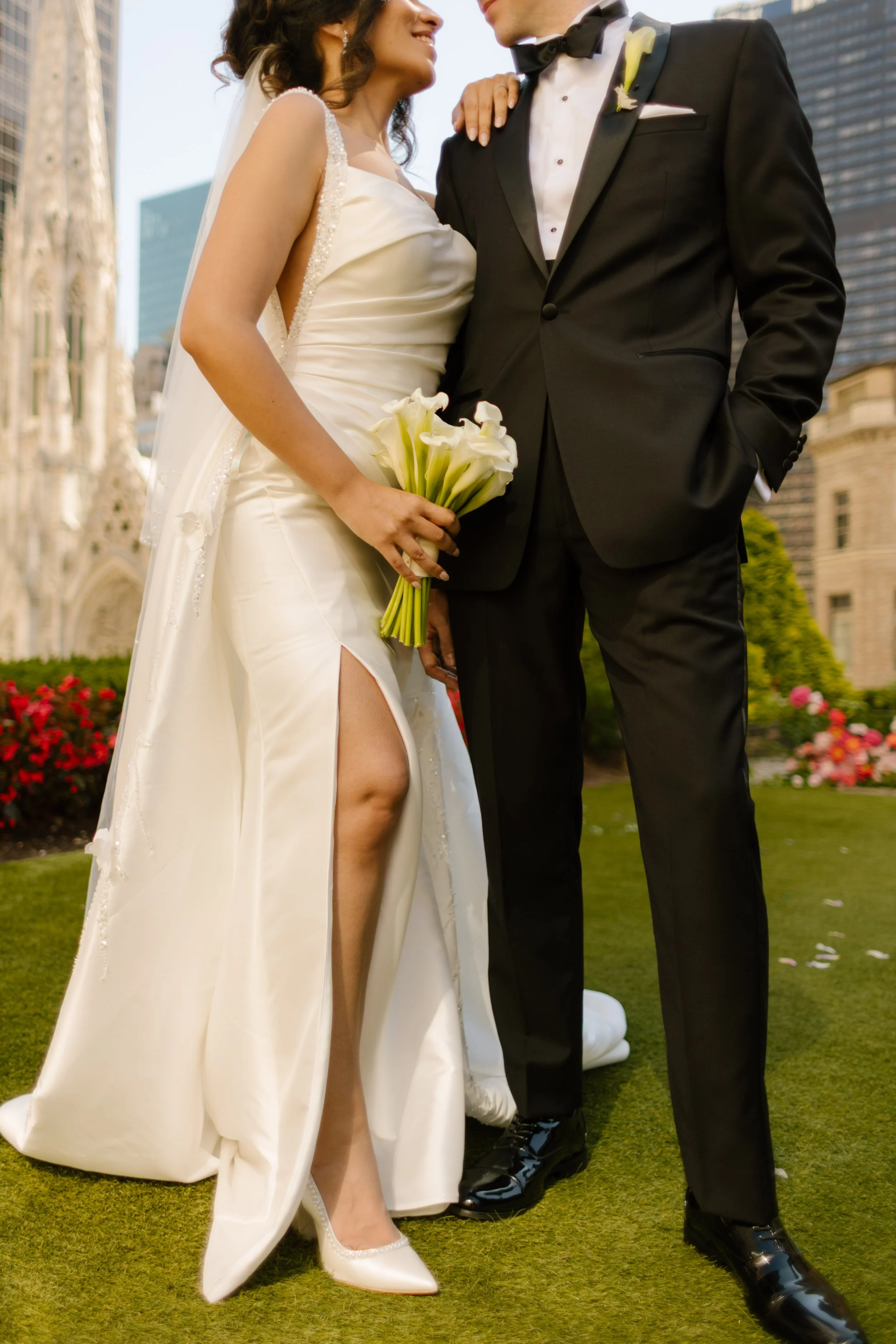 A close-up of the couple holding hands and a bouquet of white calla lilies, St. Patrick’s Cathedral and the city skyline rising behind them