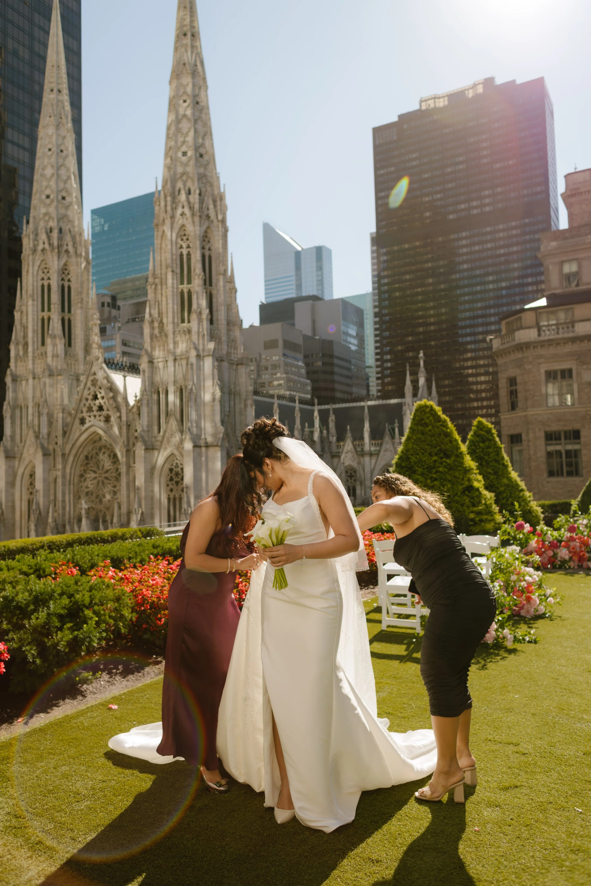 The bride gets a final adjustment to her dress from her bridesmaids under the morning sun, with St. Patrick’s Cathedral rising beside her