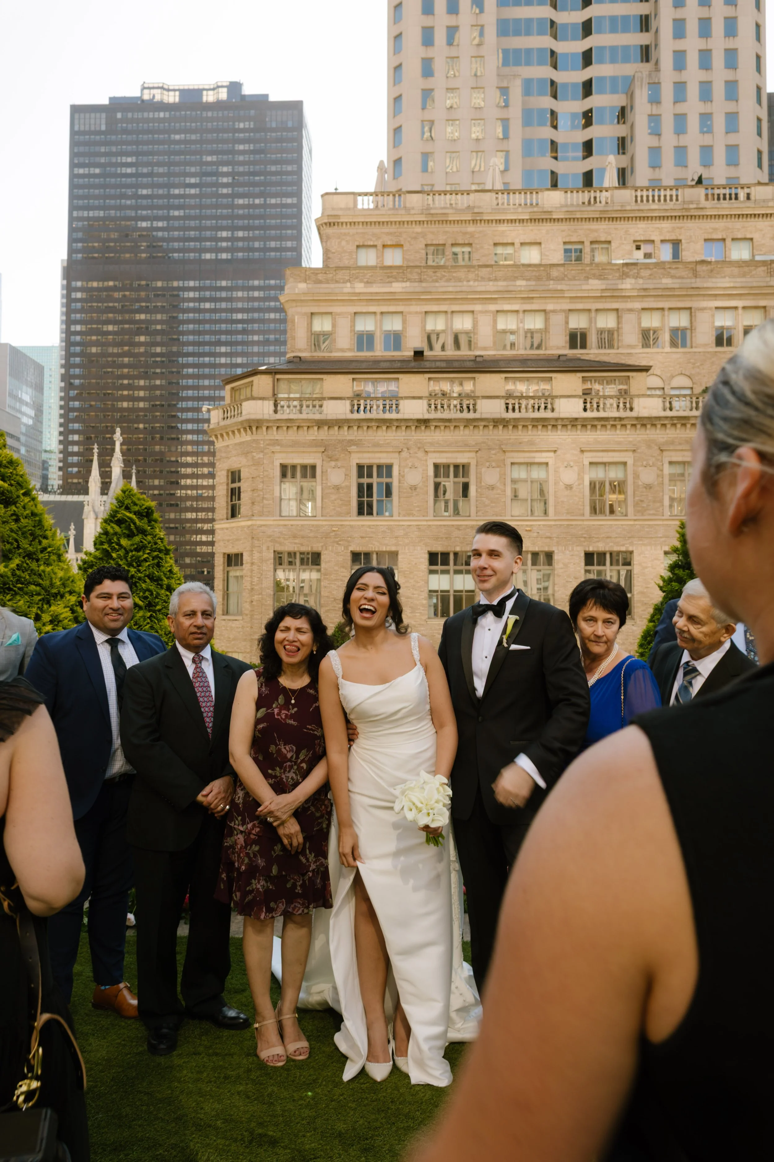 The bride laughs with her family gathered close around her and the groom, joy radiating through the frame on a sunlit rooftop during their wedding in New York City.