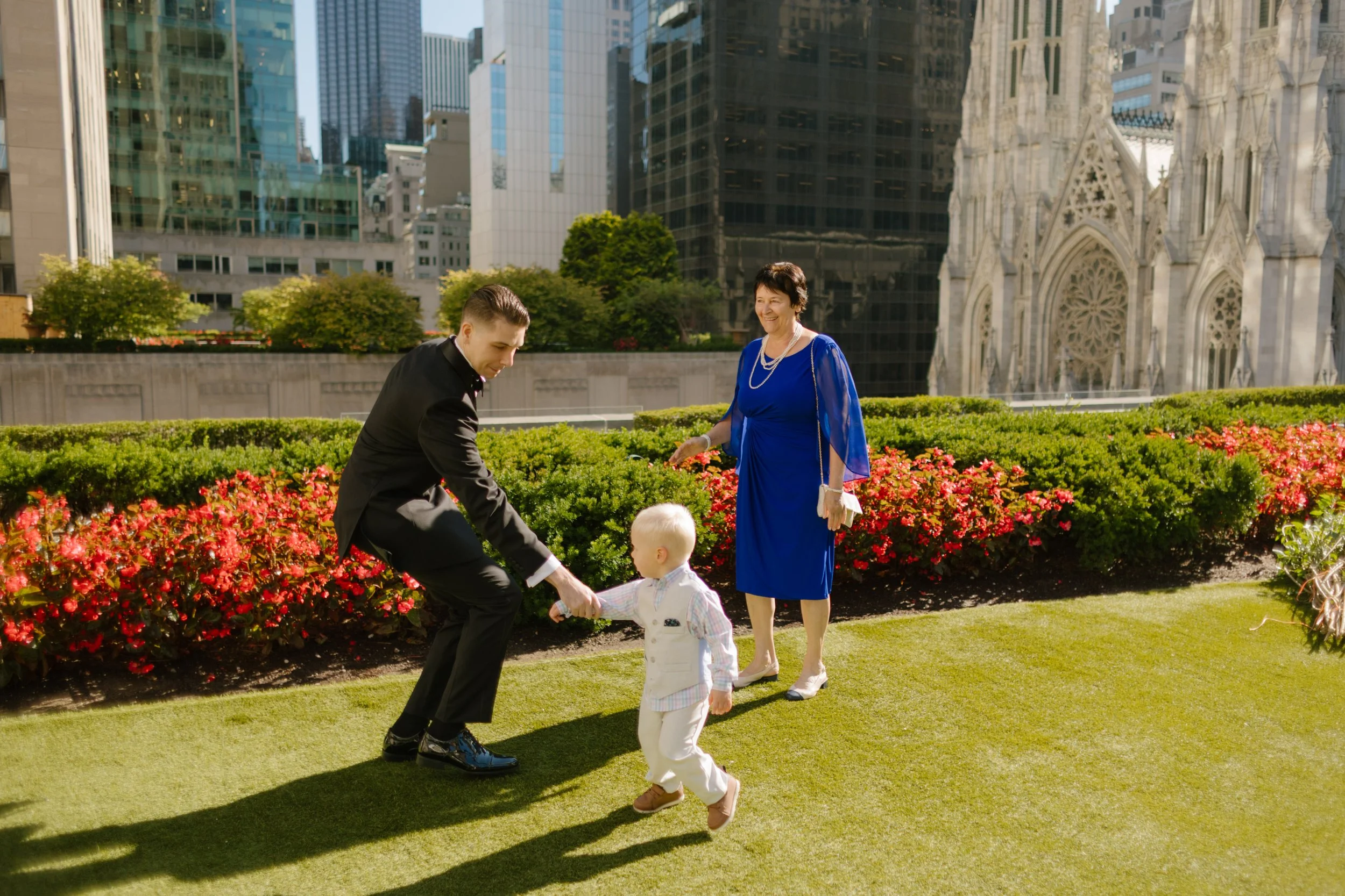The groom bends down to greet a toddler mid-run, with the bride’s mother smiling nearby—sweet, chaotic family energy blooming on the rooftop at their wedding in New York City.