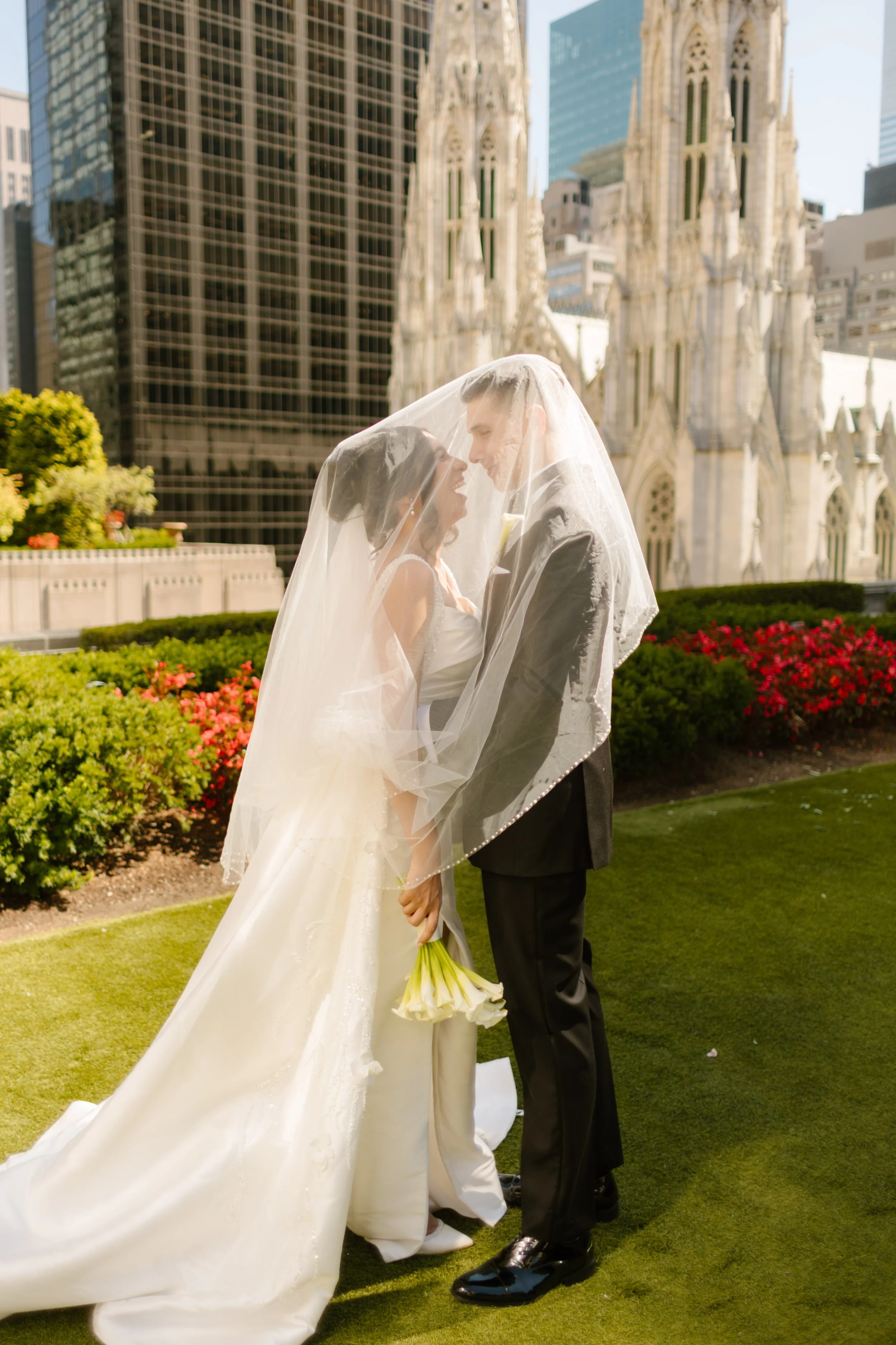 Bride and groom wrapped in a sheer veil, laughing softly beneath the city skyline—St. Patrick’s Cathedral towering behind them as they savor their wedding in New York City.