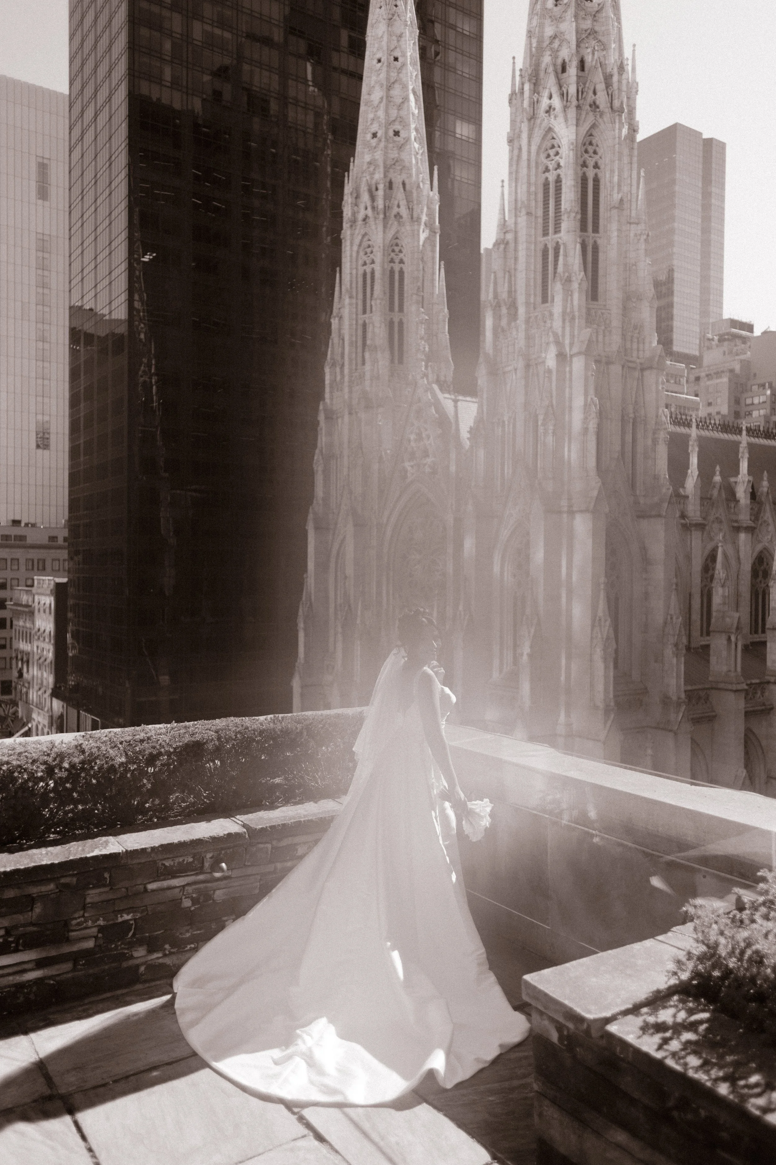 A dreamy, sepia-toned photo of the bride standing quietly with her bouquet, the dramatic towers of St. Patrick’s Cathedral glowing in the haze—timeless beauty during her wedding in New York City.